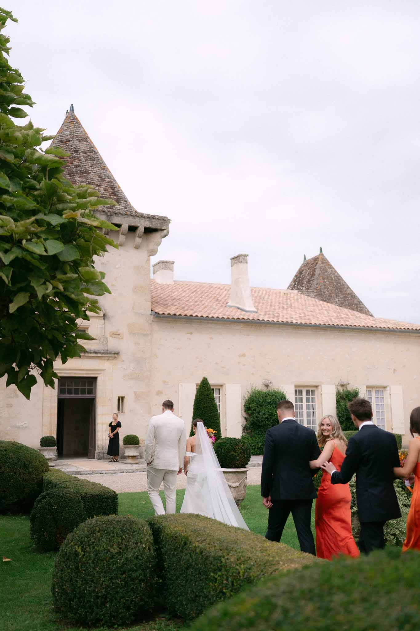 Couple walking toward turreted chateau from behind, bride in cathedral veil with orange and pink bouquet