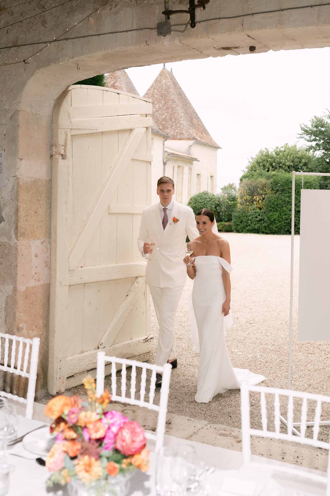 Bride and groom entering reception through stone archway with bold coral and pink floral centerpiece