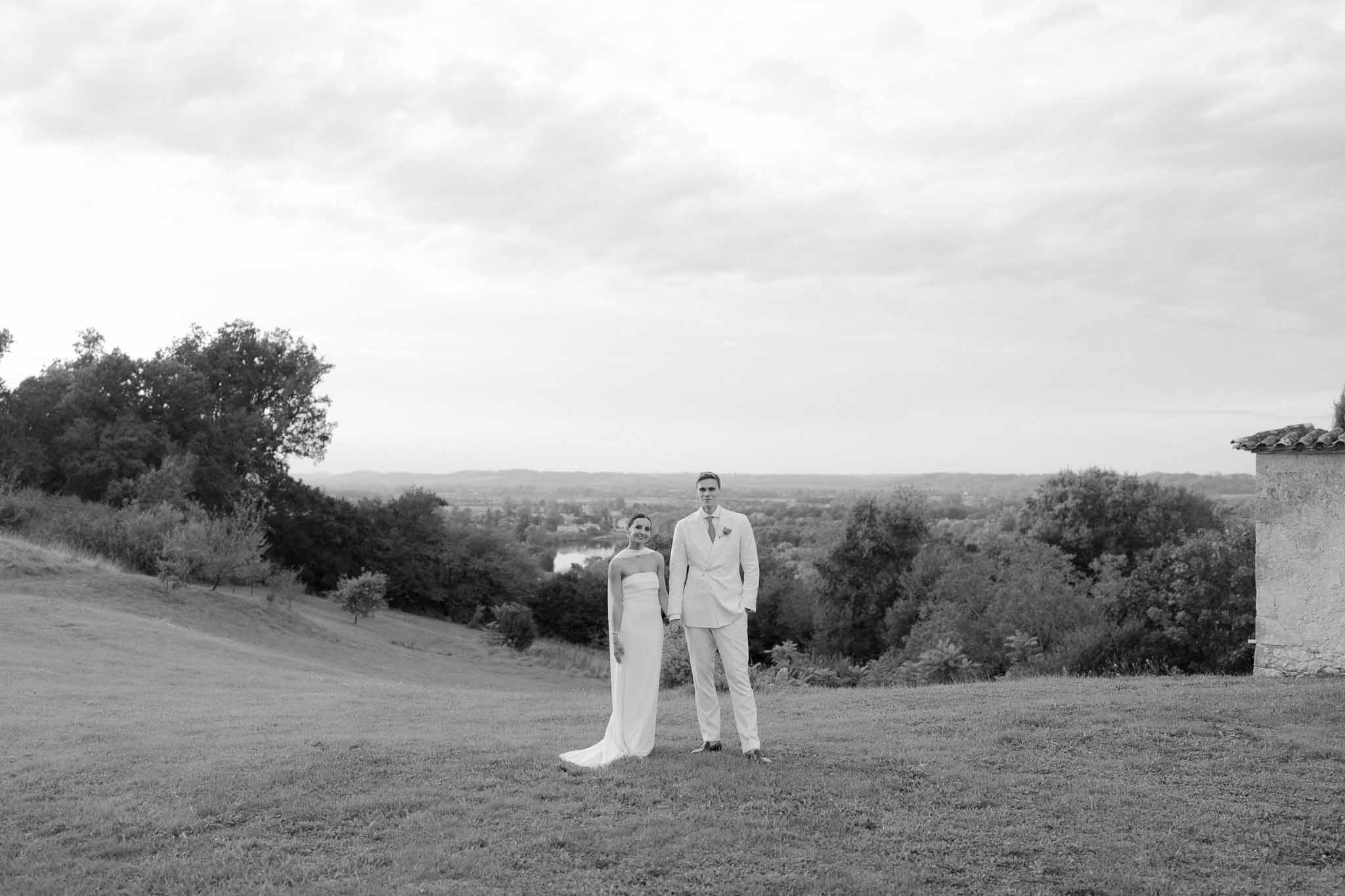 Black and white wide-angle portrait of bride and groom holding hands on a hillside overlooking a valley