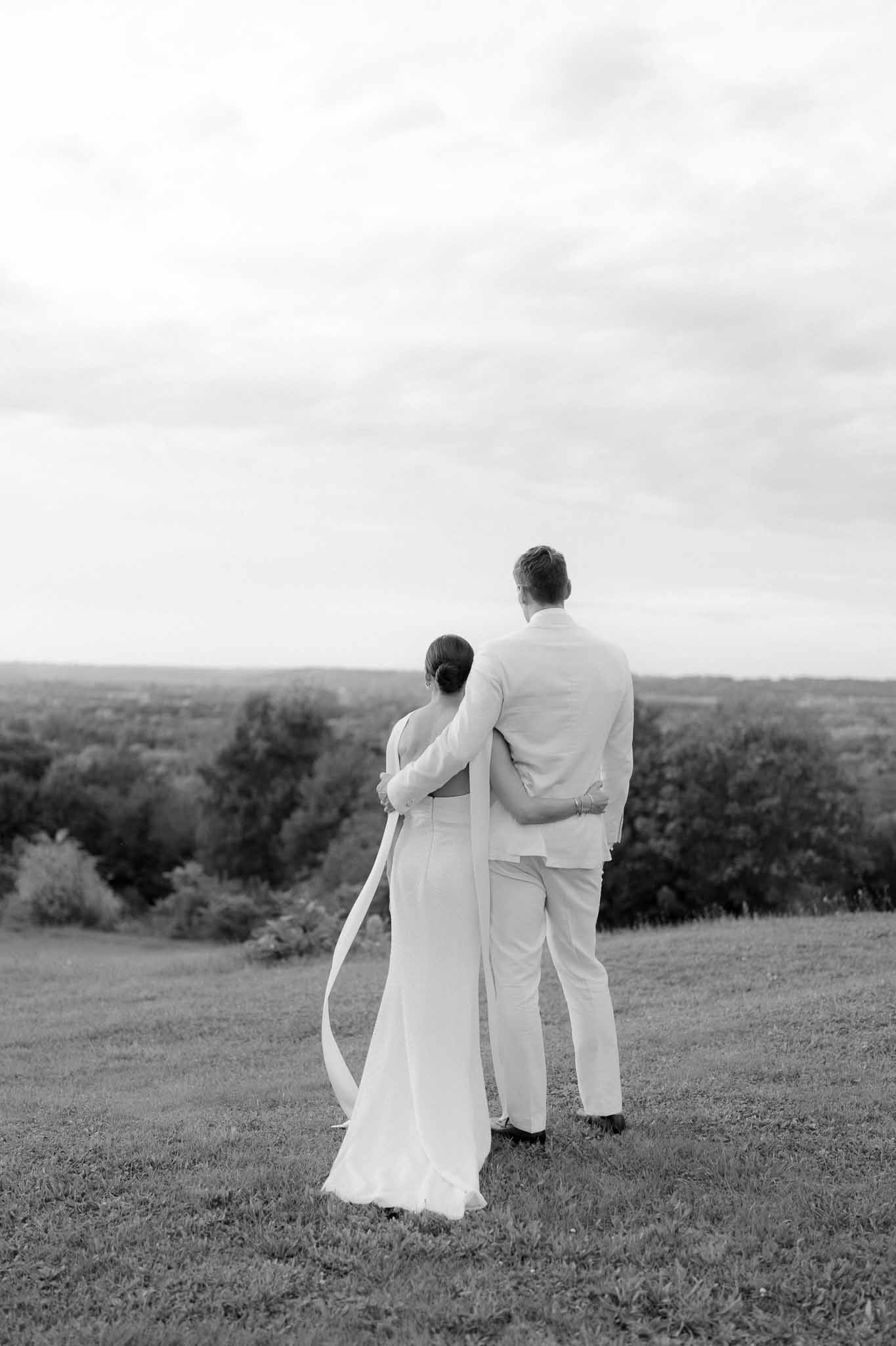 Black and white rear portrait of couple gazing over open landscape from elevated lawn