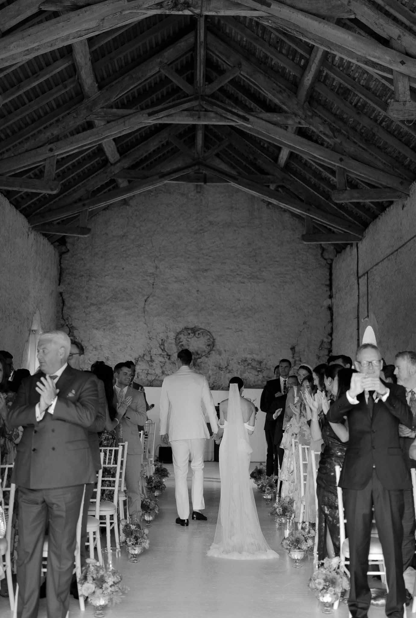 Black and white recessional in rustic barn with exposed beams as 40 guests applaud