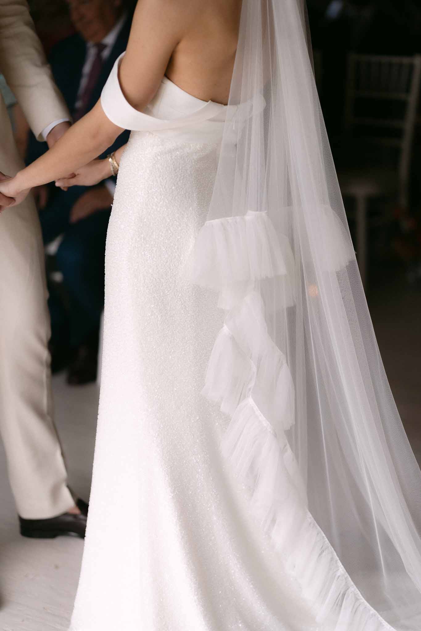 Close-up of bride's back in strapless sequined gown with cathedral veil featuring petal applique detailing