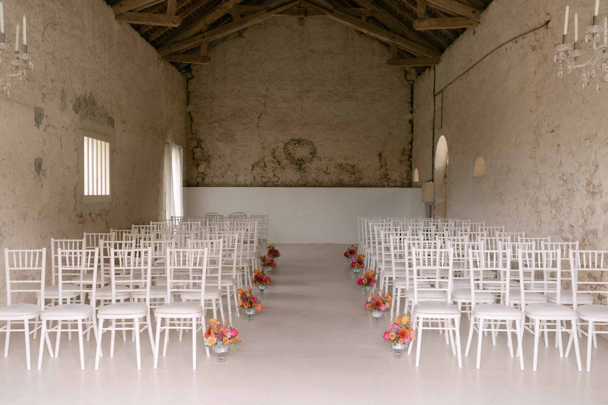 Whitewashed barn ceremony with chiavari chairs and vibrant orange and hot pink aisle arrangements