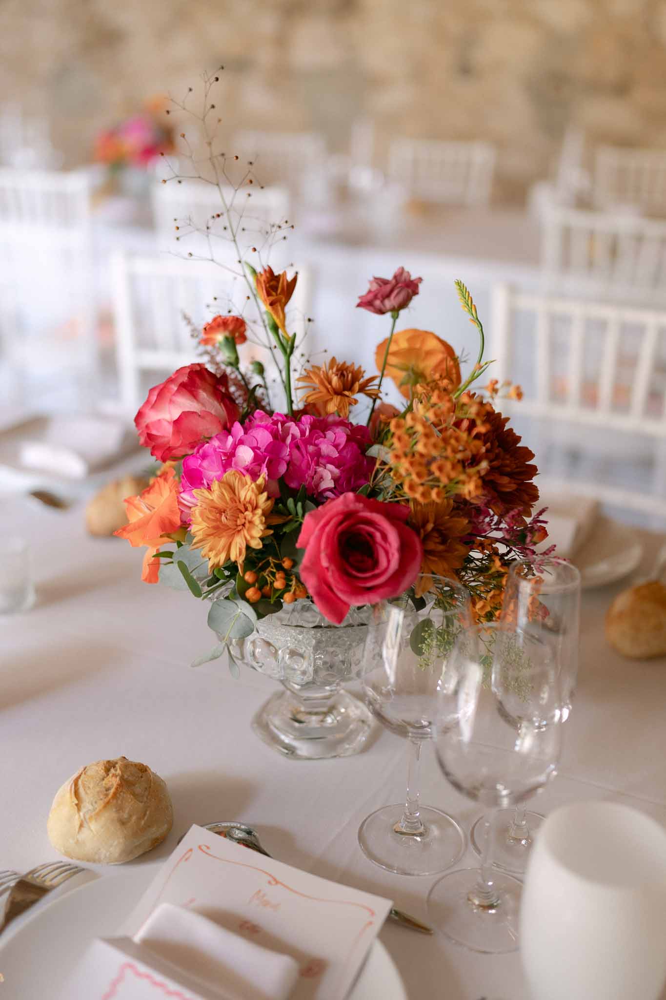 Reception centerpiece in glass compote vase with hot pink roses, orange dahlias, and fuchsia hydrangeas