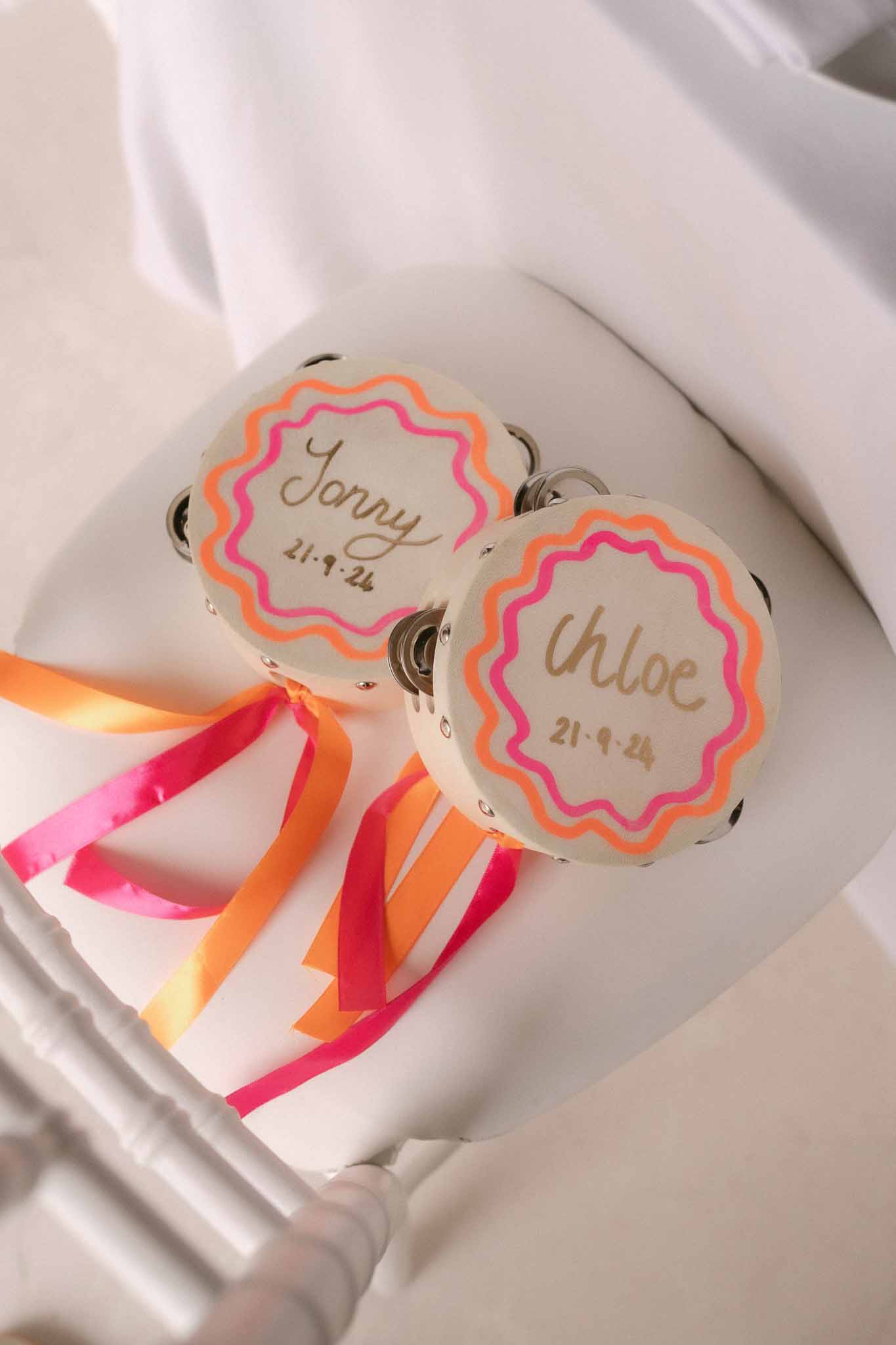 Personalised mini tambourines with hot pink and orange ribbons and gold script guest names