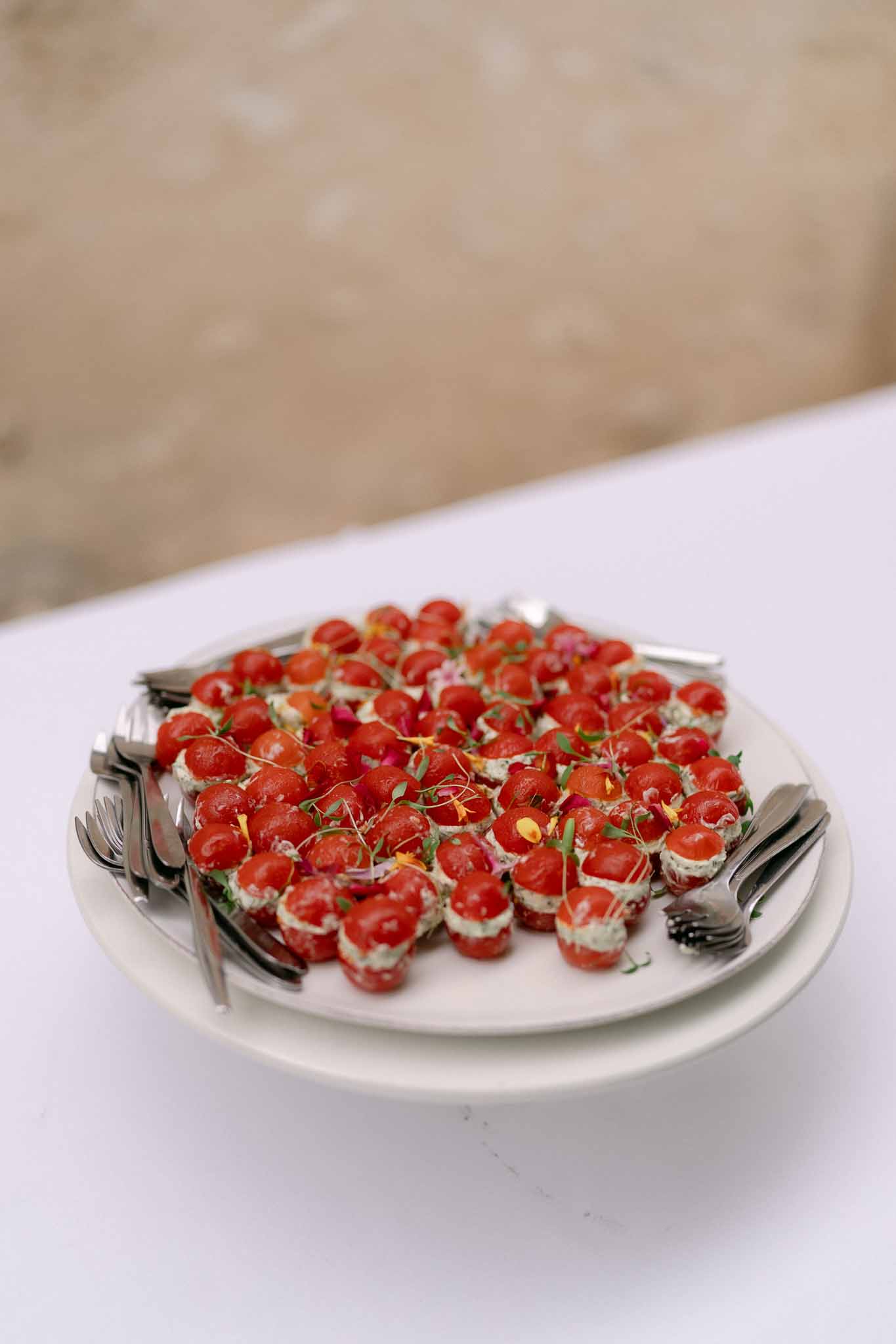 Round white platter of stuffed cherry tomato canapes with microgreens and edible flower petals on white linen