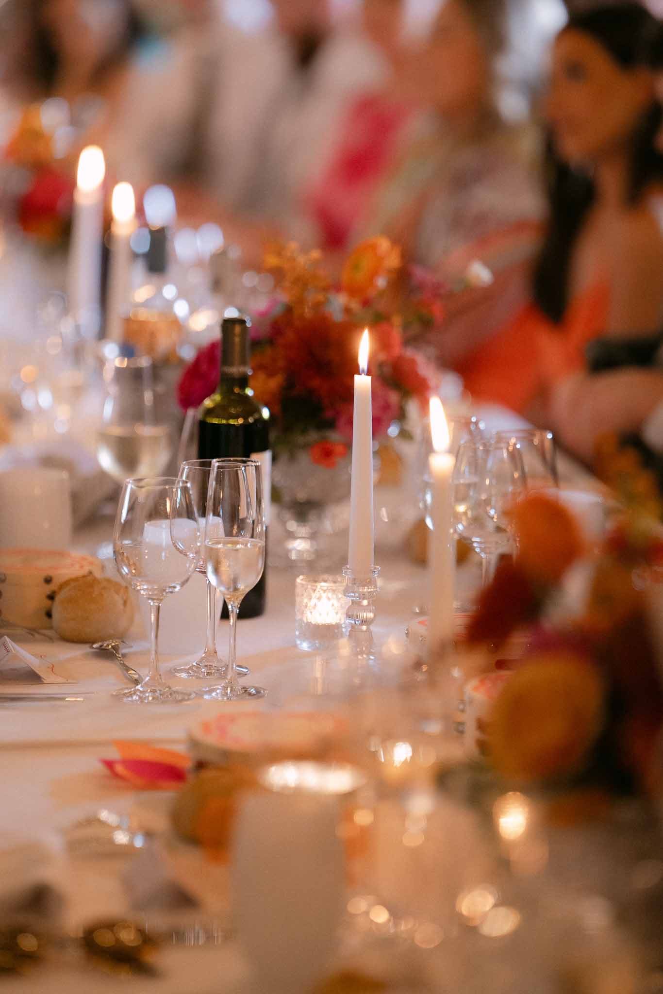 Reception table detail with coral and hot pink ranunculus centerpieces, taper candles, and white linens