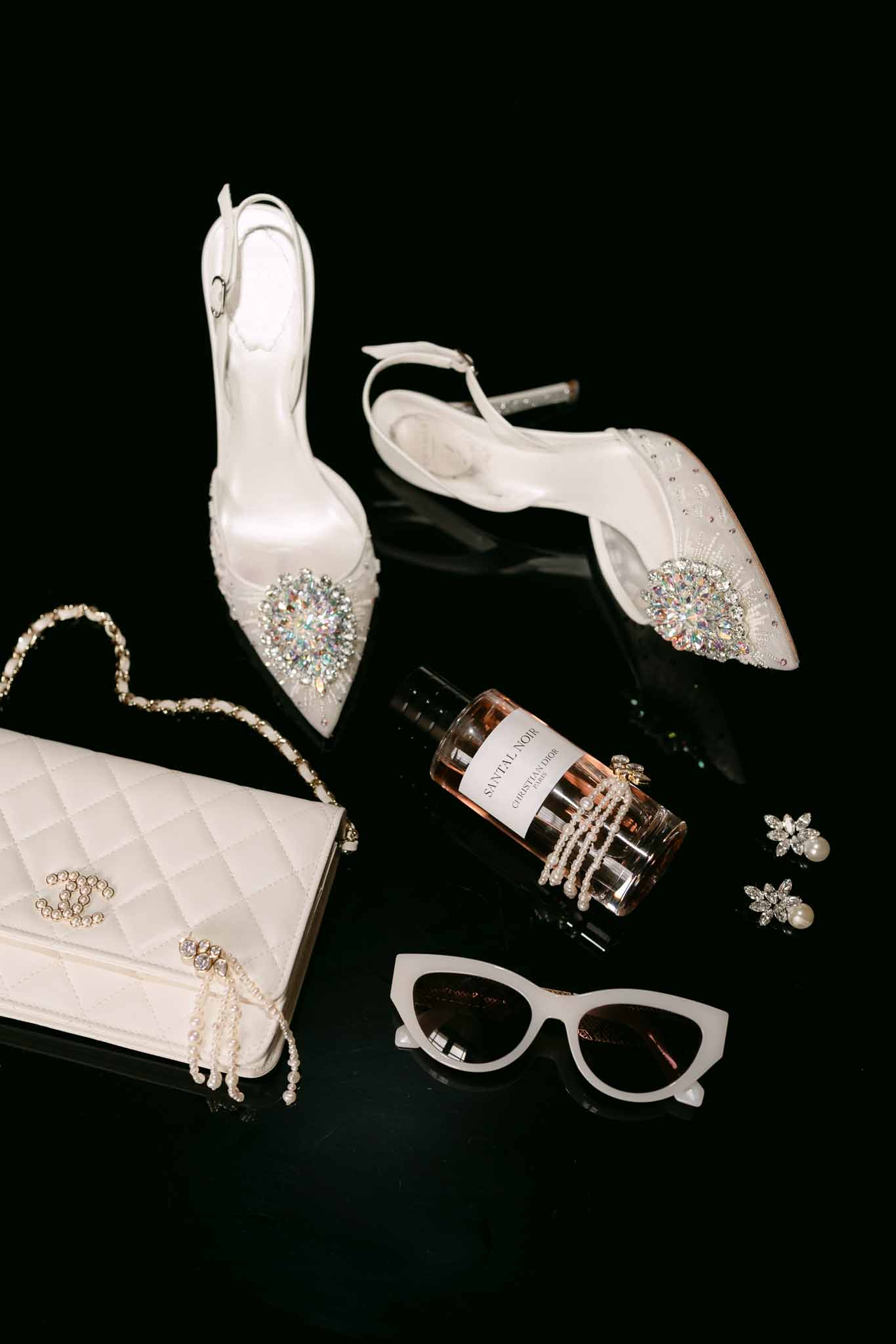 Bridal flat lay with crystal slingback heels, white Chanel bag, Dior fragrance, and pearl accessories