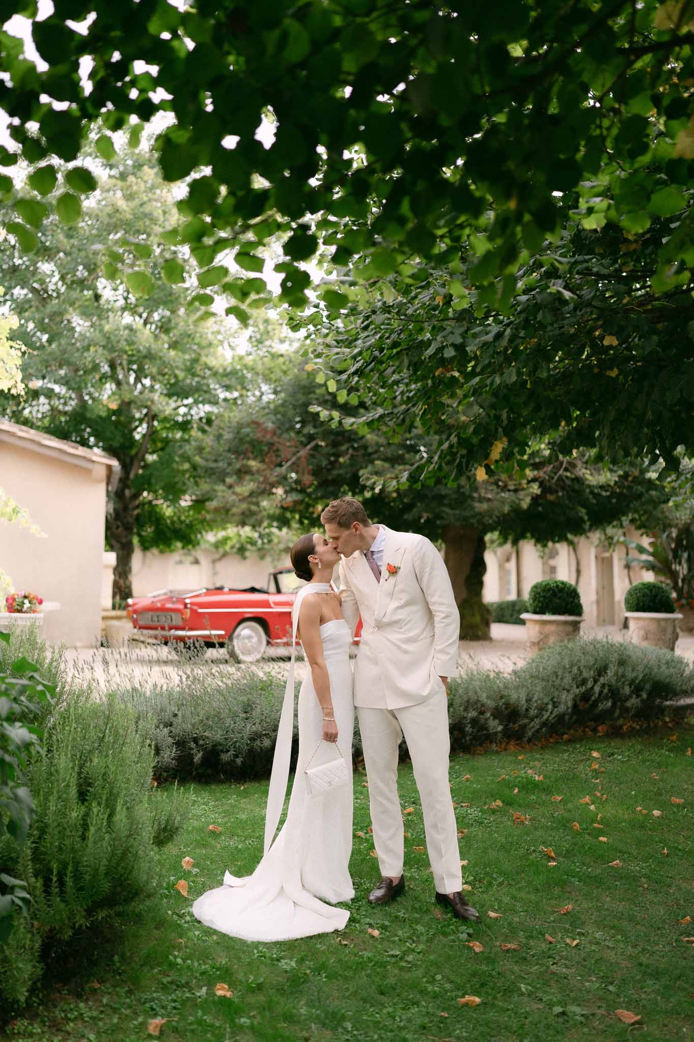 Bride and groom kissing beside vintage red convertible on chateau gravel drive