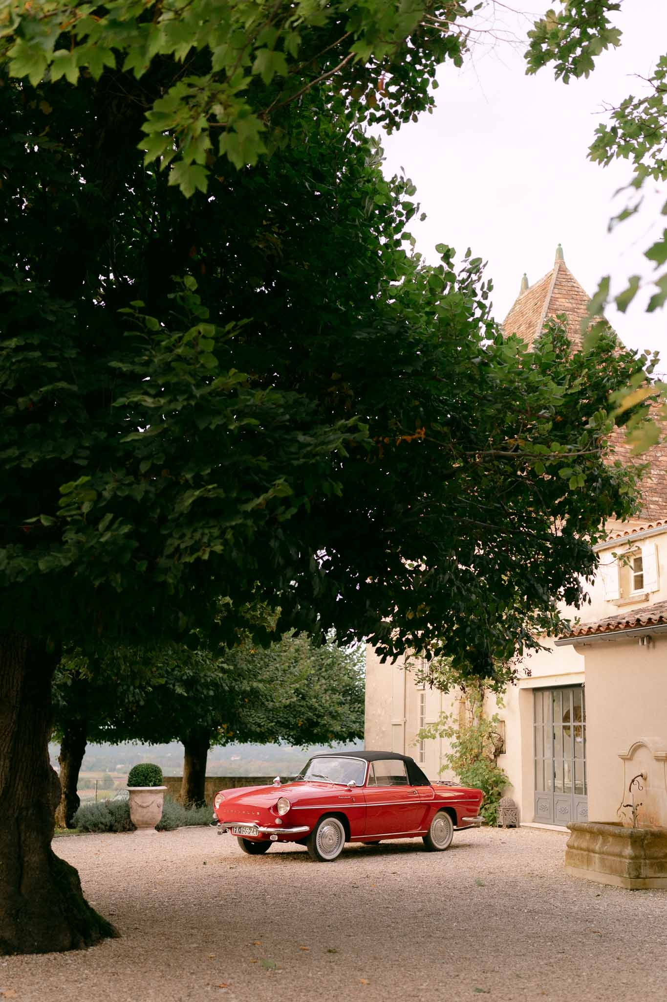 Vintage red convertible parked on chateau gravel courtyard with pointed turret in background