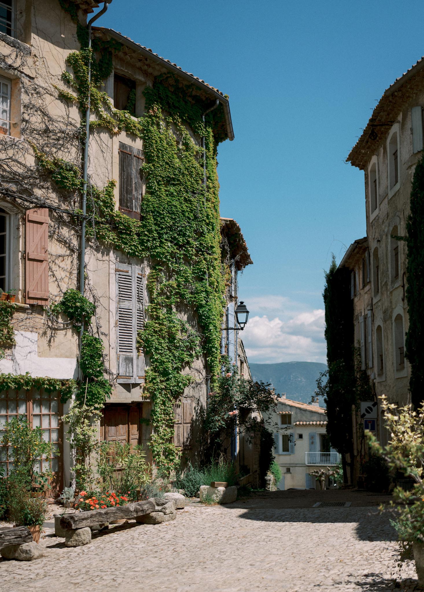 Cobblestone street in a Provencal village with stone buildings, wooden shutters, and distant mountain view