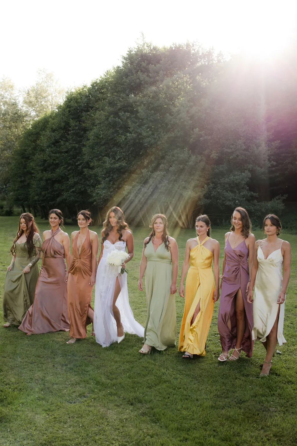 Bride and bridesmaids group portrait on lawn with hedge backdrop during golden hour