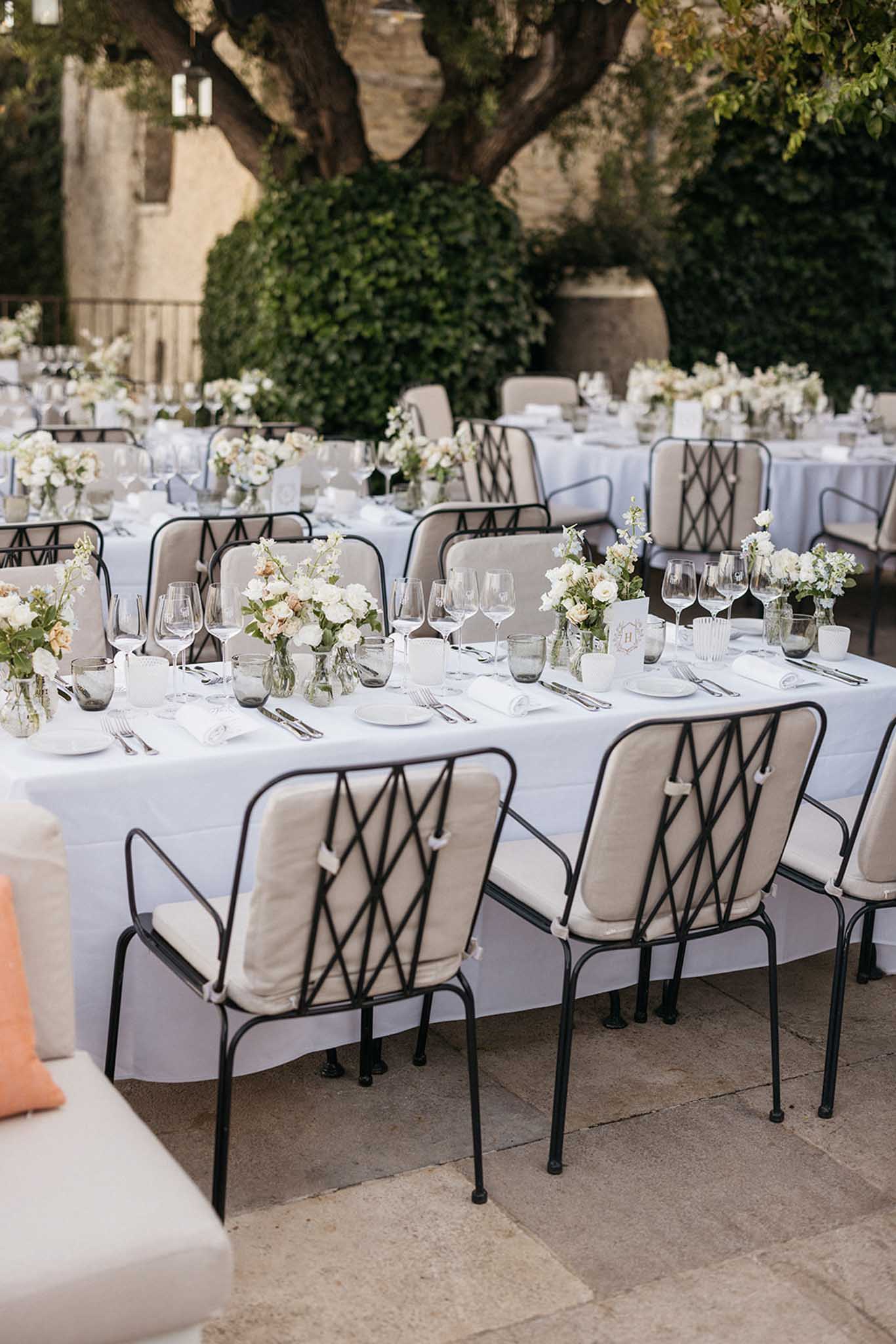 Outdoor reception table setting with white linens and floral centerpieces in ivy-covered courtyard
