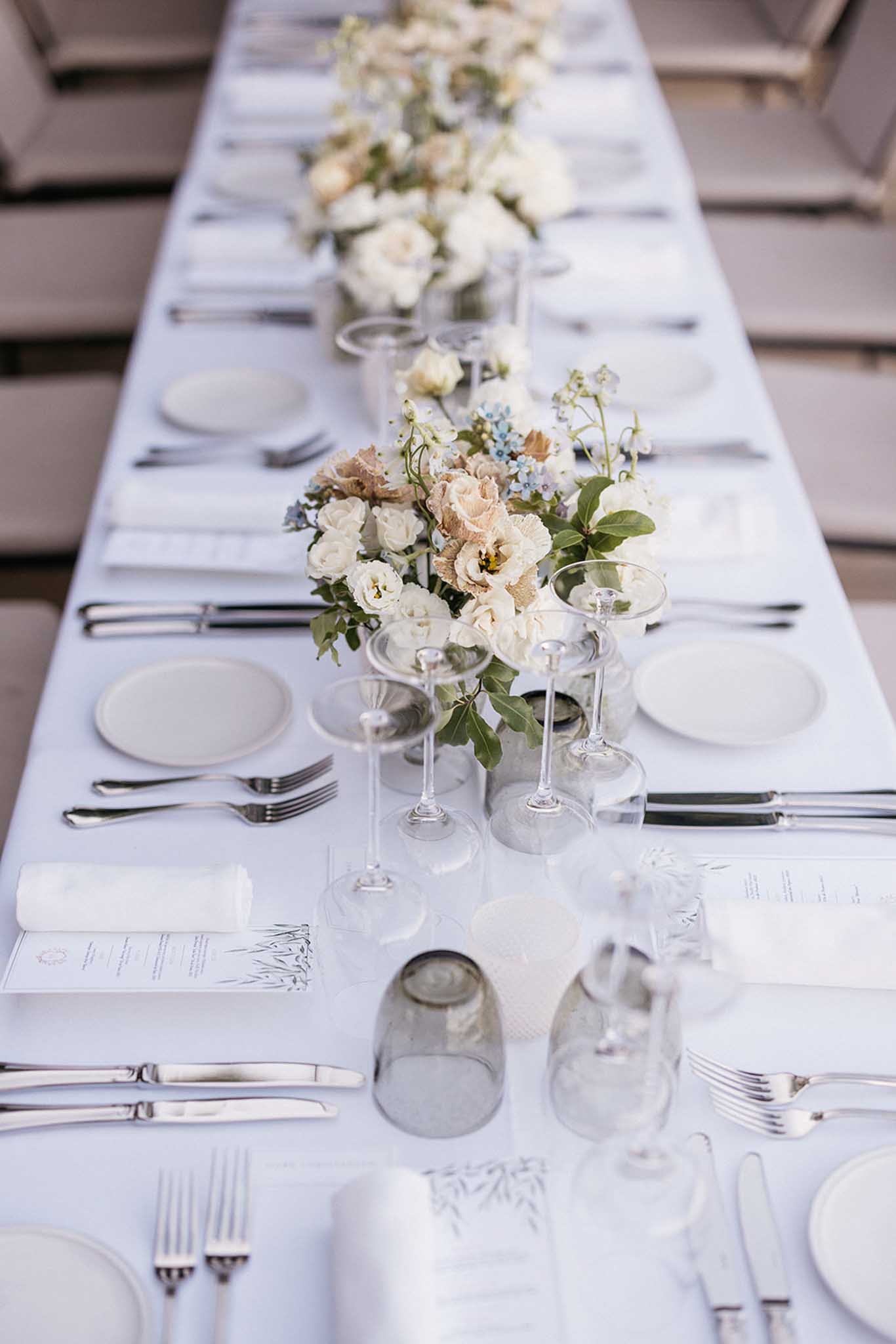 Long banquet table with floral centerpieces and formal place settings at indoor wedding reception