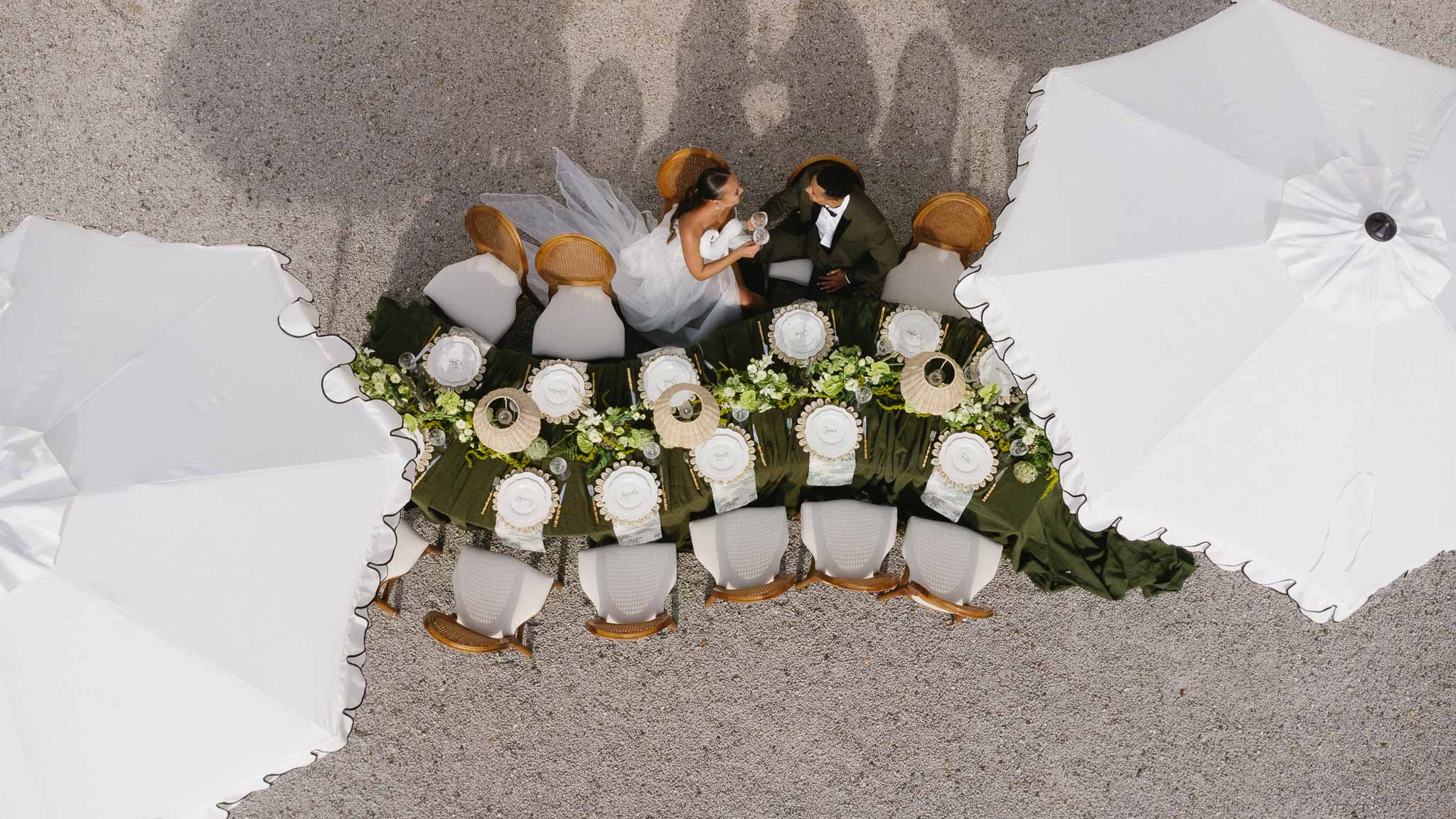 Aerial view of bride and groom dining at elegant reception table with white florals and gold accents