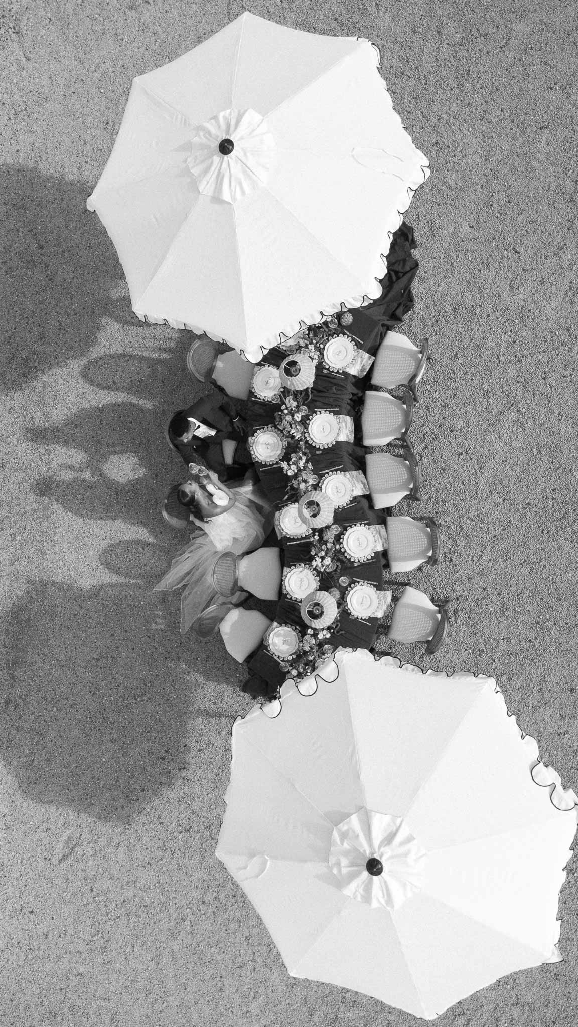 Aerial view of wedding reception table with umbrellas and guests at outdoor venue