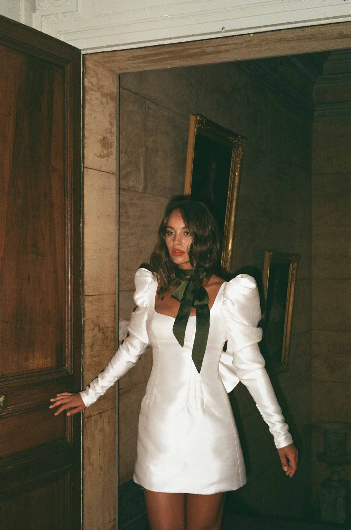 Bride in short white dress with green tie in vintage interior doorway