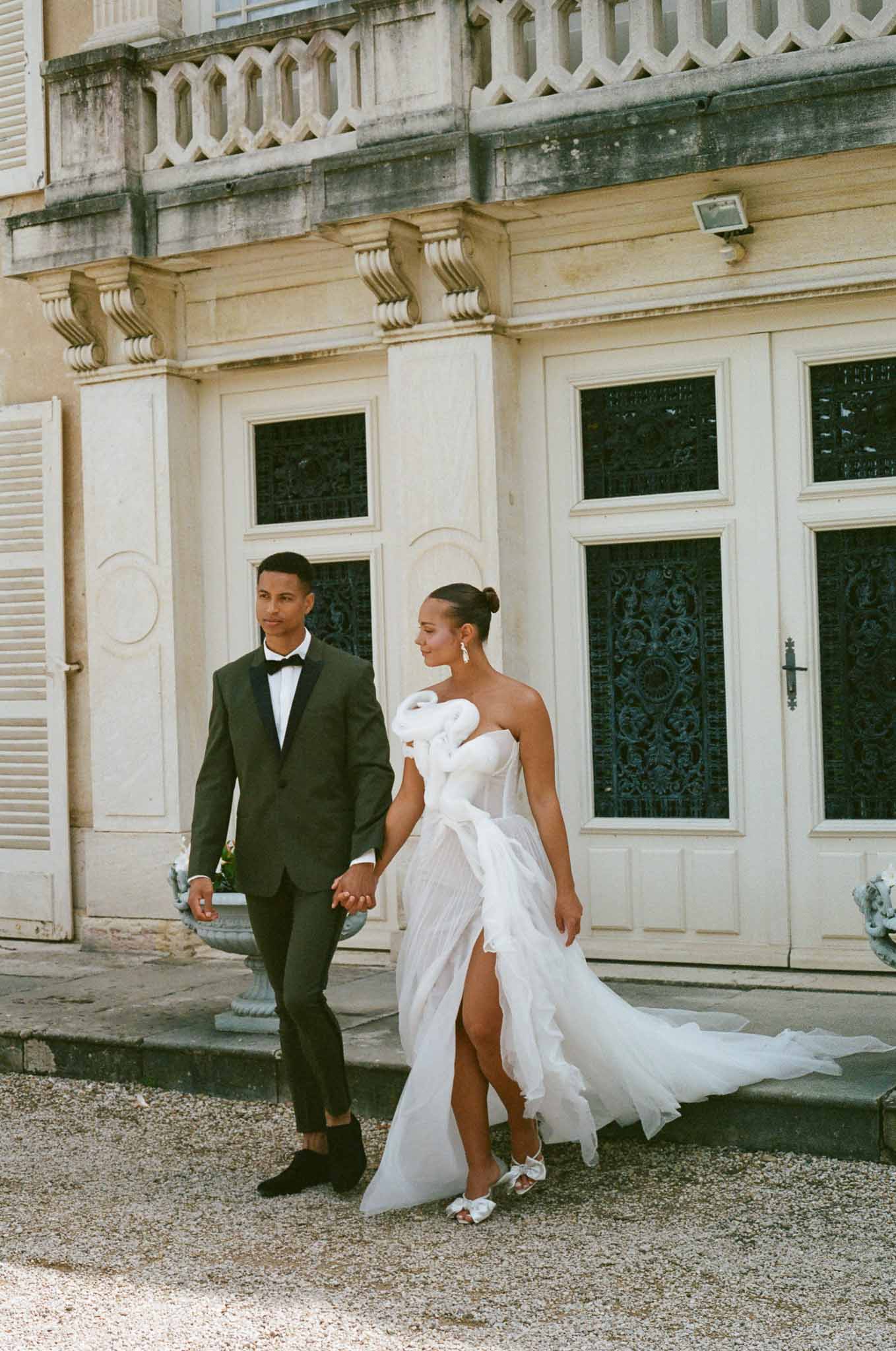 Bride and groom walking hand-in-hand across courtyard at classical stone château