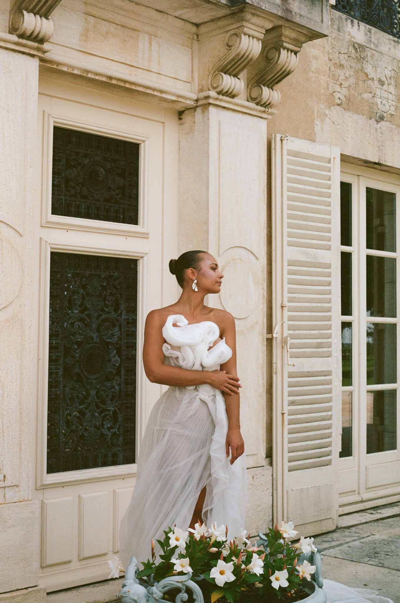 Bride in sculptural white dress with pearl earrings at historic stone courtyard with ornate architectural details