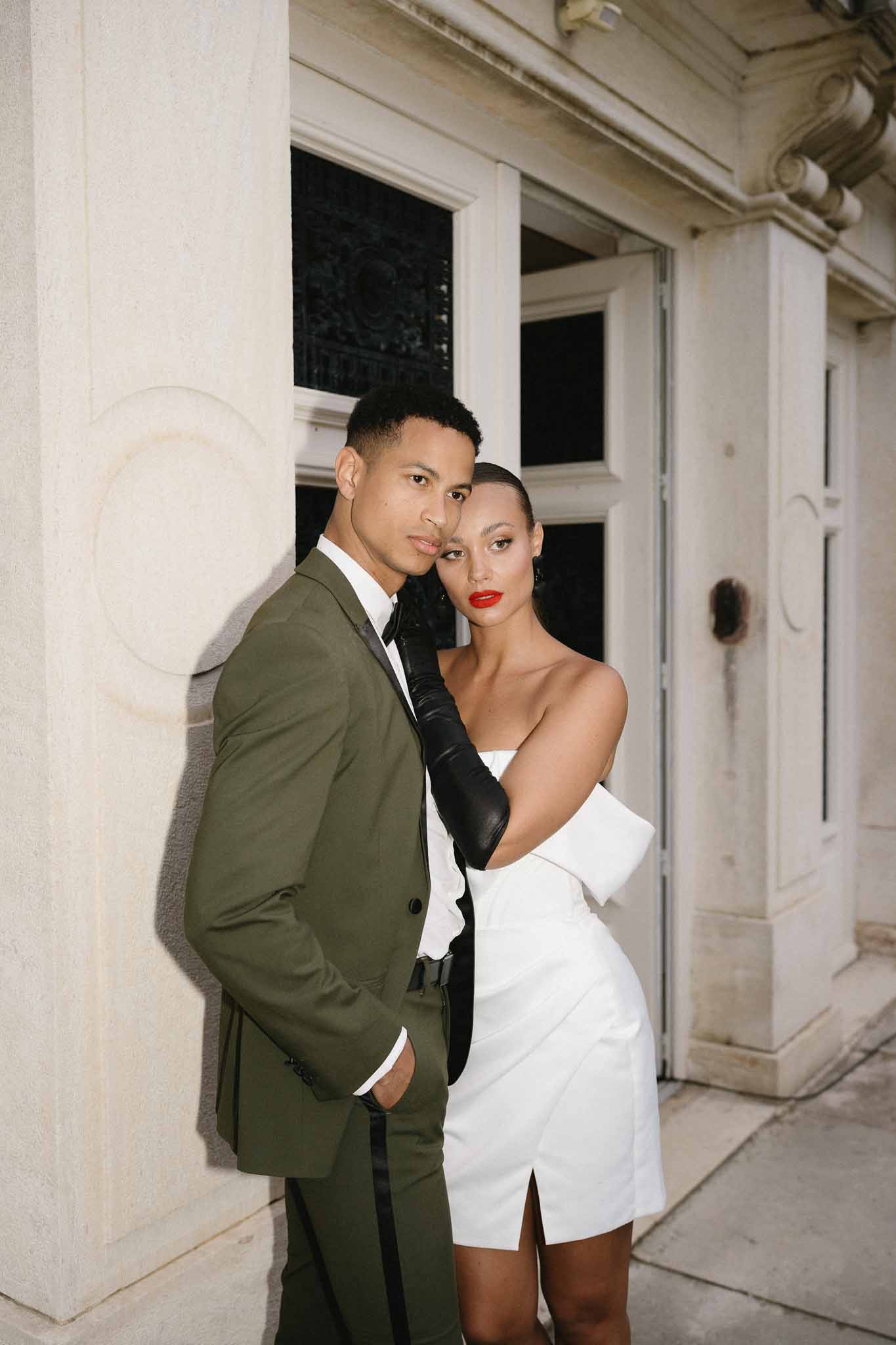 Couple in modern wedding attire posing at night outside classical stone building with columns