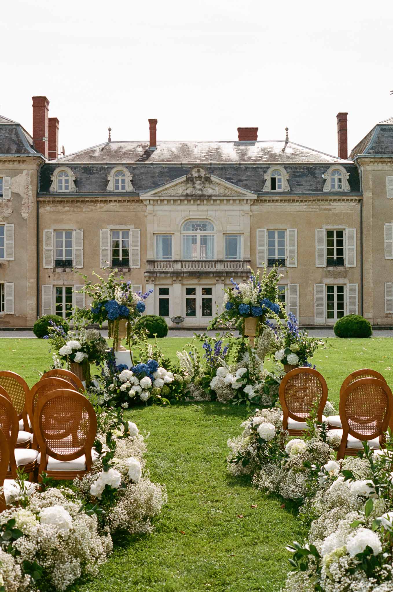 Outdoor wedding ceremony setup on lawn of classical French chateau with floral aisle arrangements
