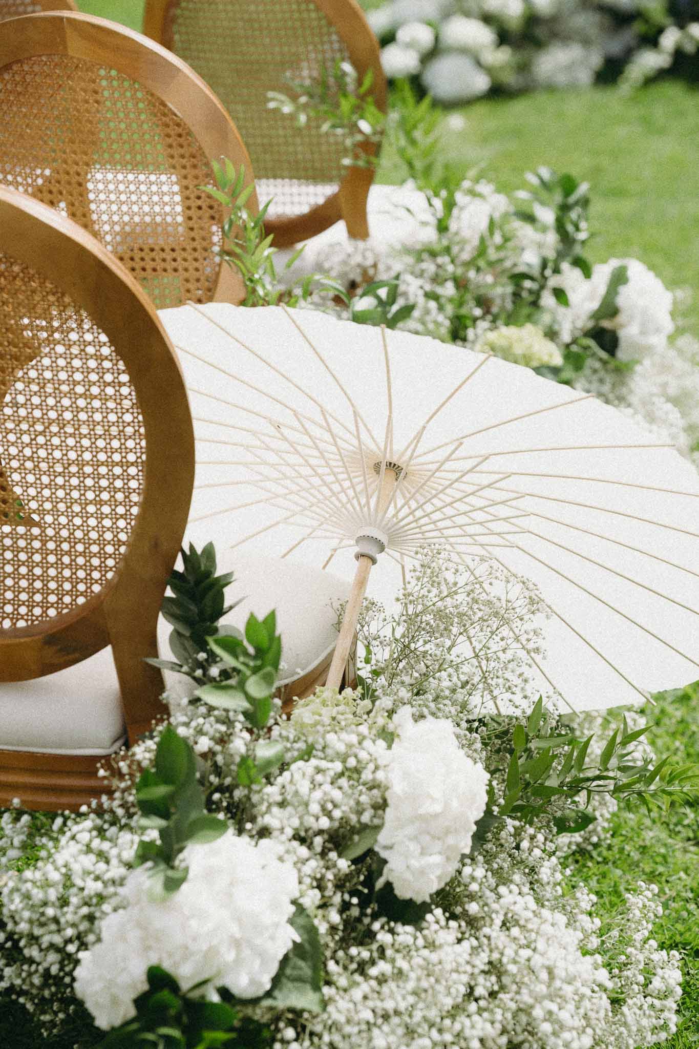 Wedding ceremony decor with cream parasols and white floral arrangements on outdoor lawn