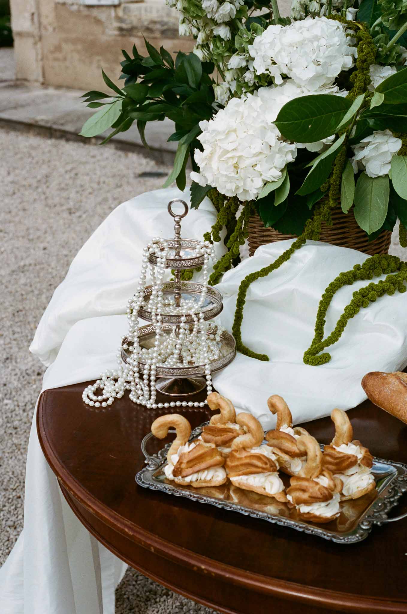 Reception table setting with silver tiered stand, pearl accents, and white hydrangea centerpiece at rustic venue