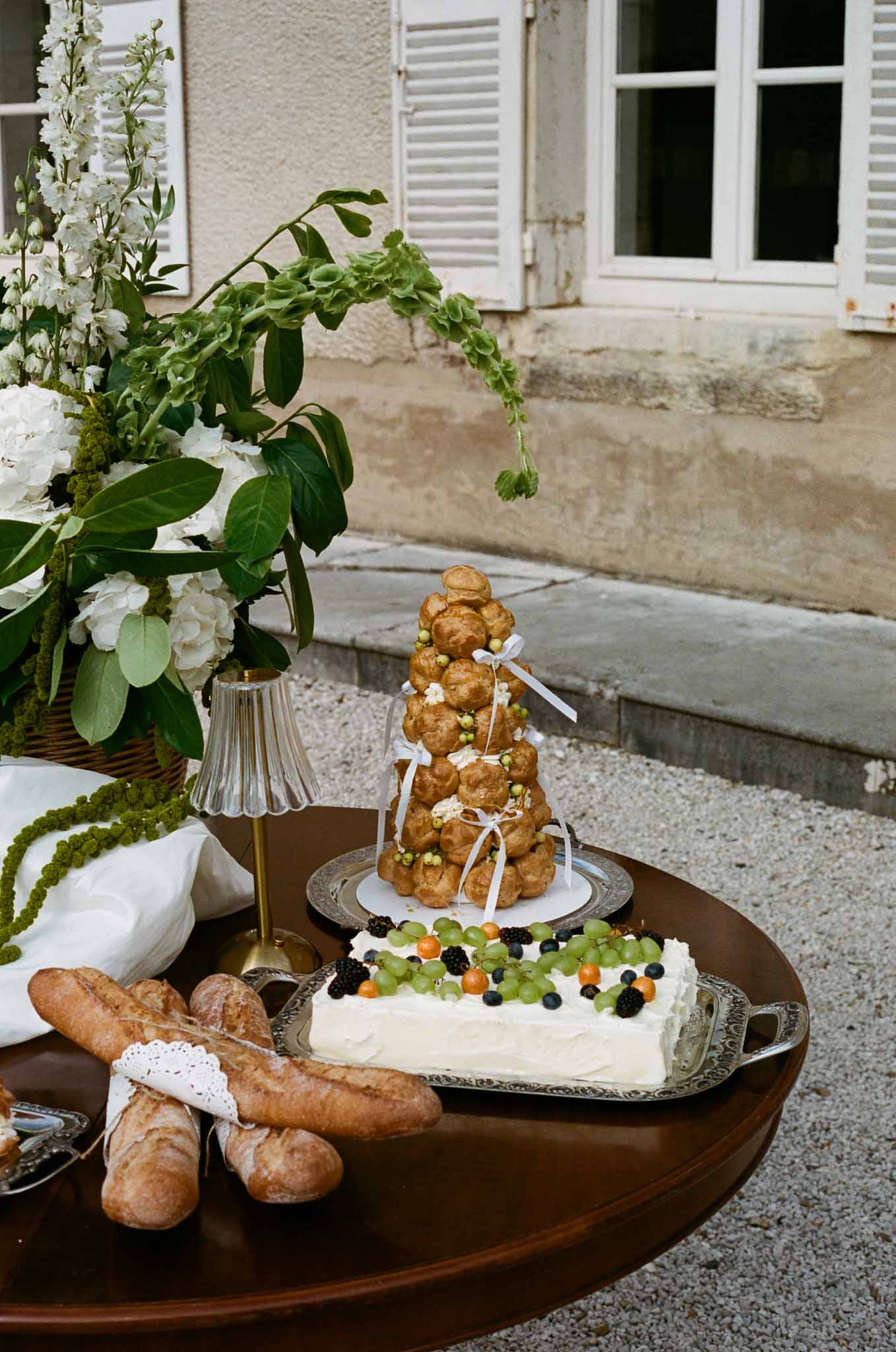 French wedding dessert display with croquembouche and decorated cake at outdoor courtyard reception