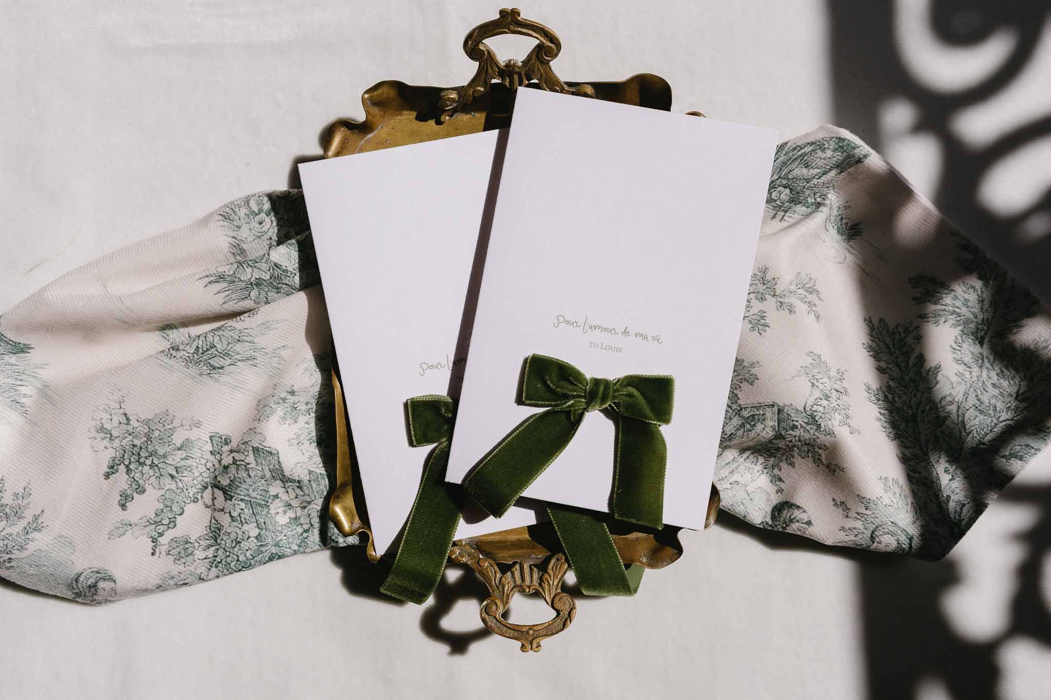 Wedding stationery flat lay with forest green velvet ribbon and toile fabric swatches on brass clipboard holders