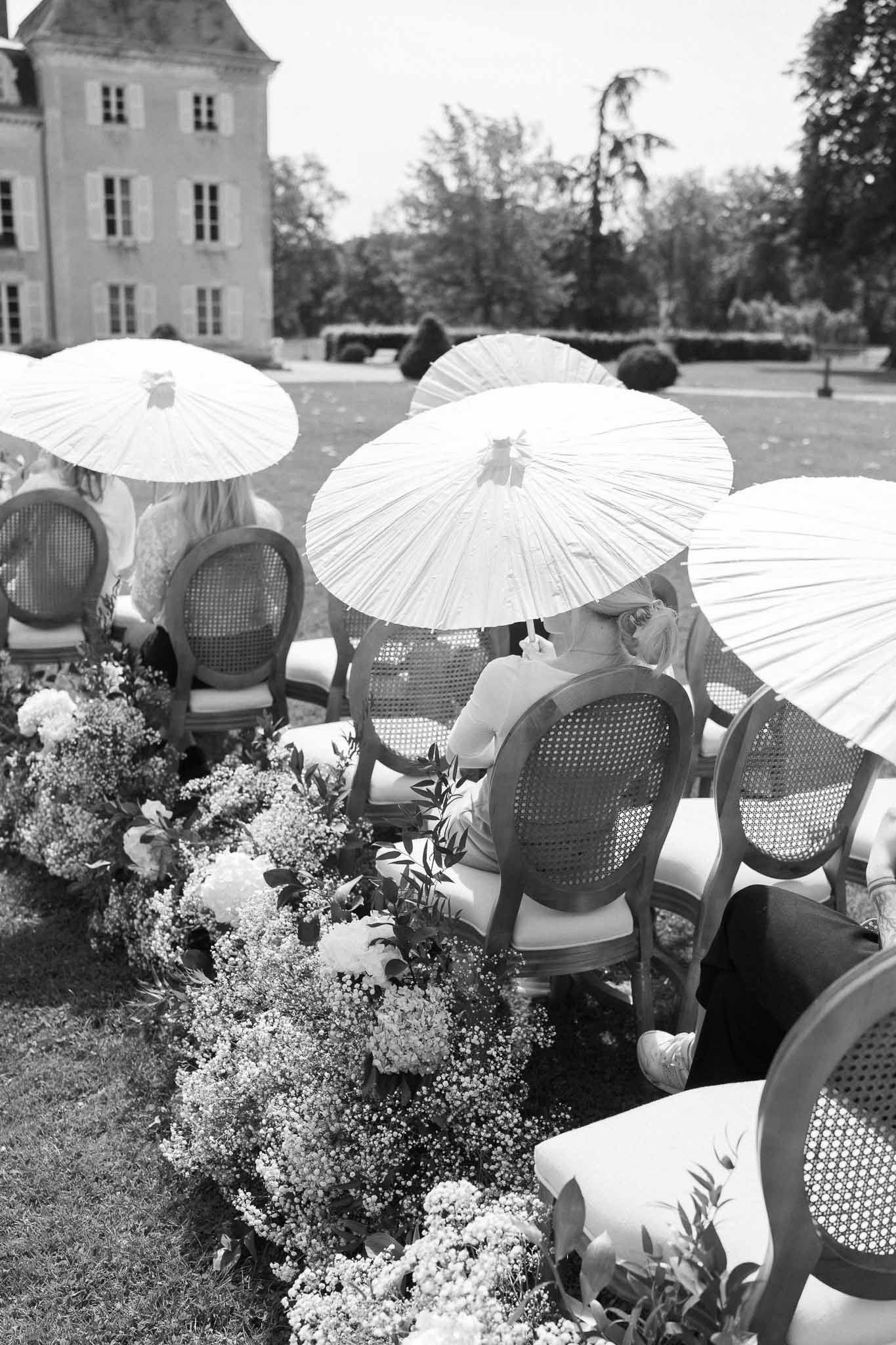 Cocktail hour guests with parasols in formal château garden setting
