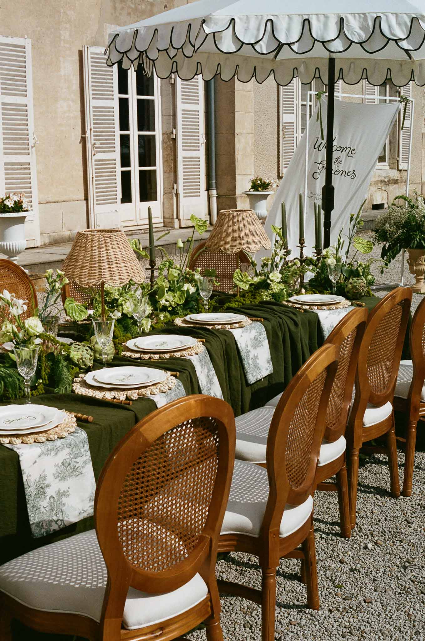 Outdoor reception table setting with green linens and botanical centerpieces in European courtyard