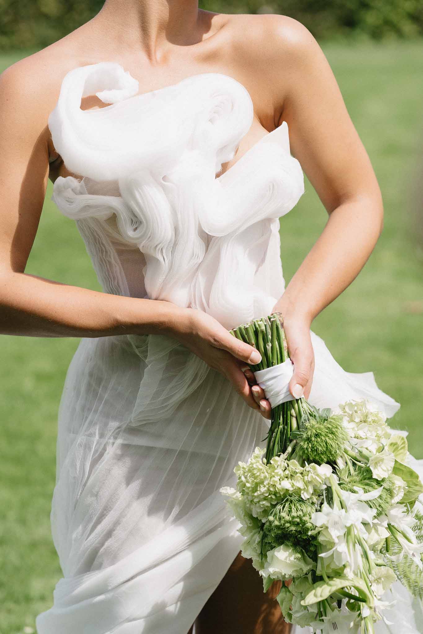 Bride holding white hydrangea bouquet in strapless wedding dress on outdoor lawn