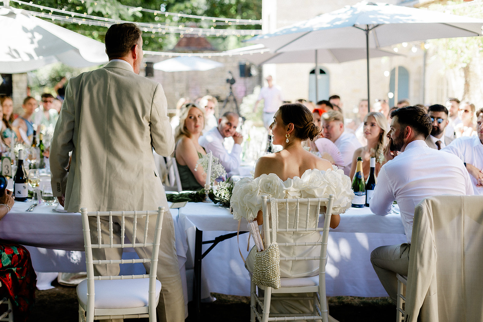 Groom giving speech during outdoor wedding reception under white marquee with string lights