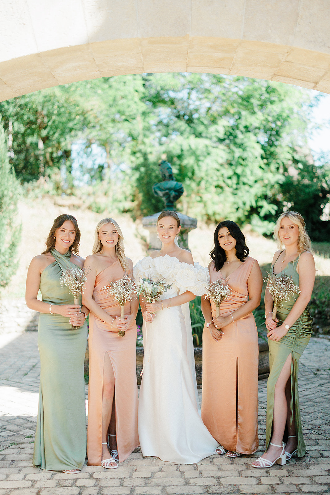 Bride and bridesmaids formal portrait under stone archway in garden courtyard