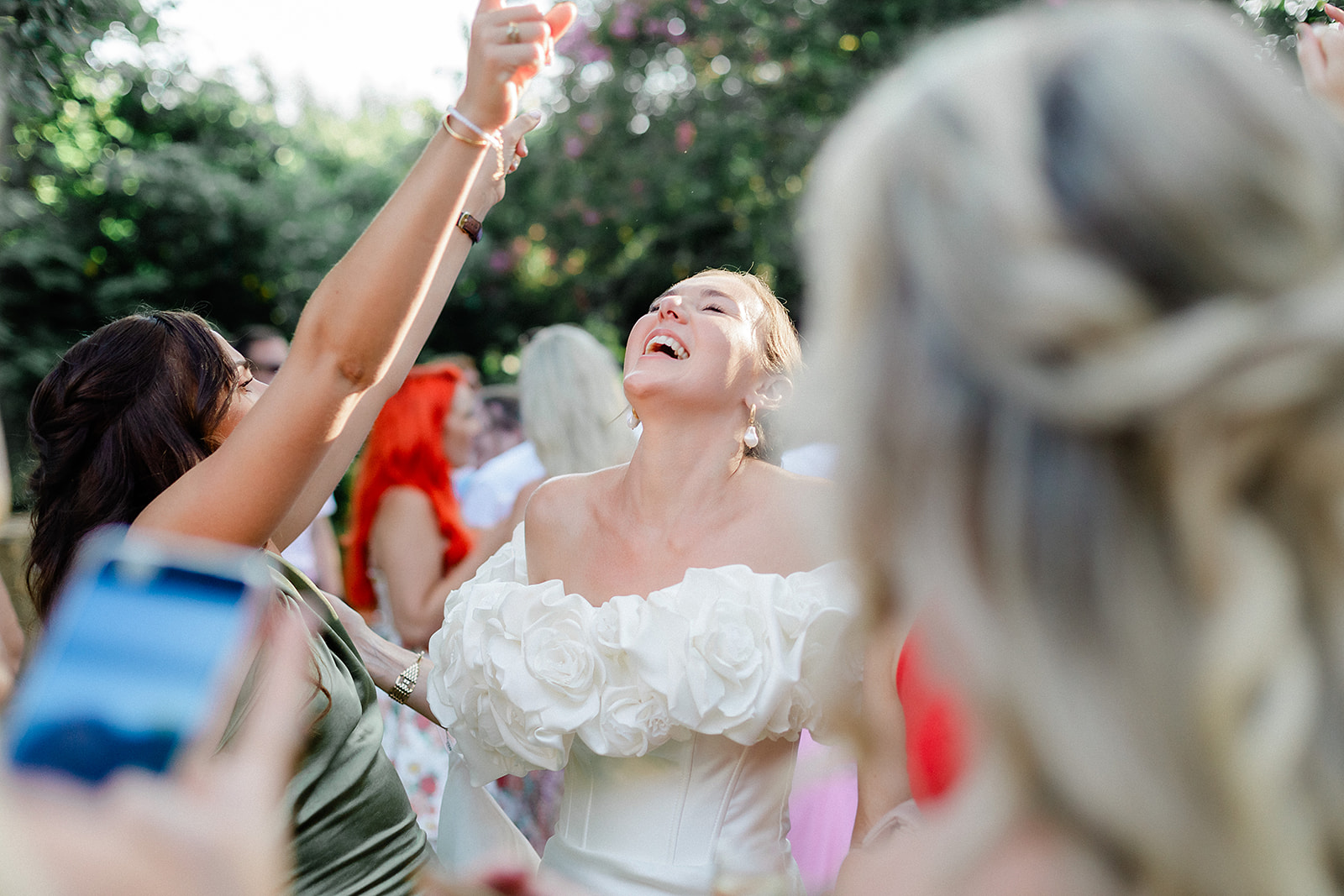 Bride dancing joyfully during outdoor garden reception with guests watching and taking photos