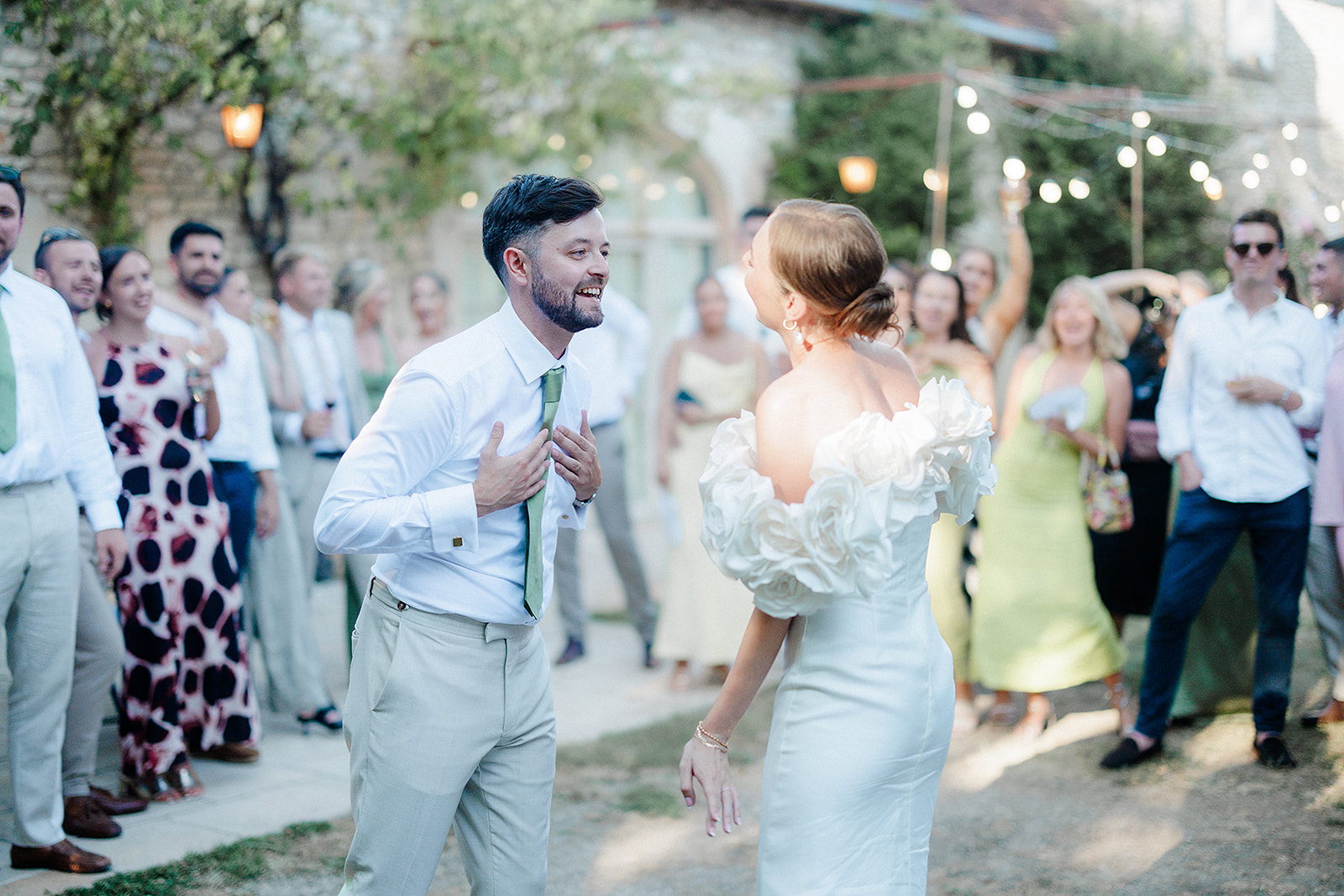 Couple's first dance surrounded by guests in outdoor courtyard reception with string lights