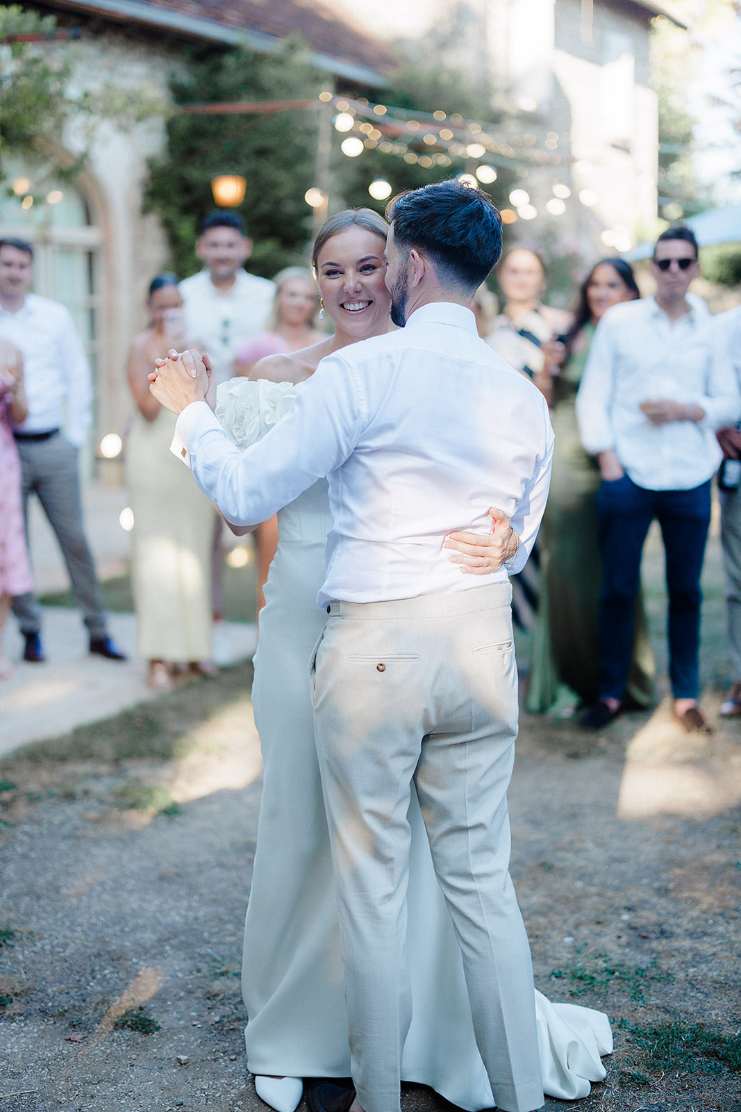 Bride and groom first dance at outdoor courtyard reception with string lights and guests watching