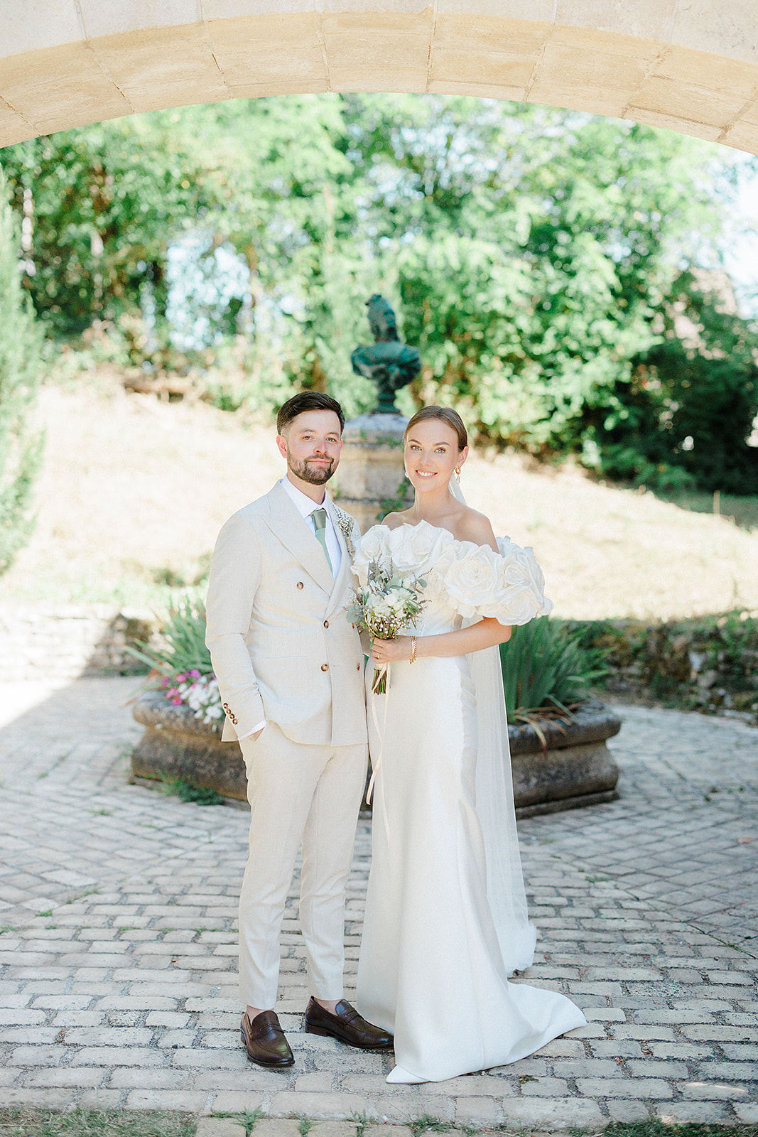 Bride and groom formal portrait beneath stone archway in garden courtyard setting