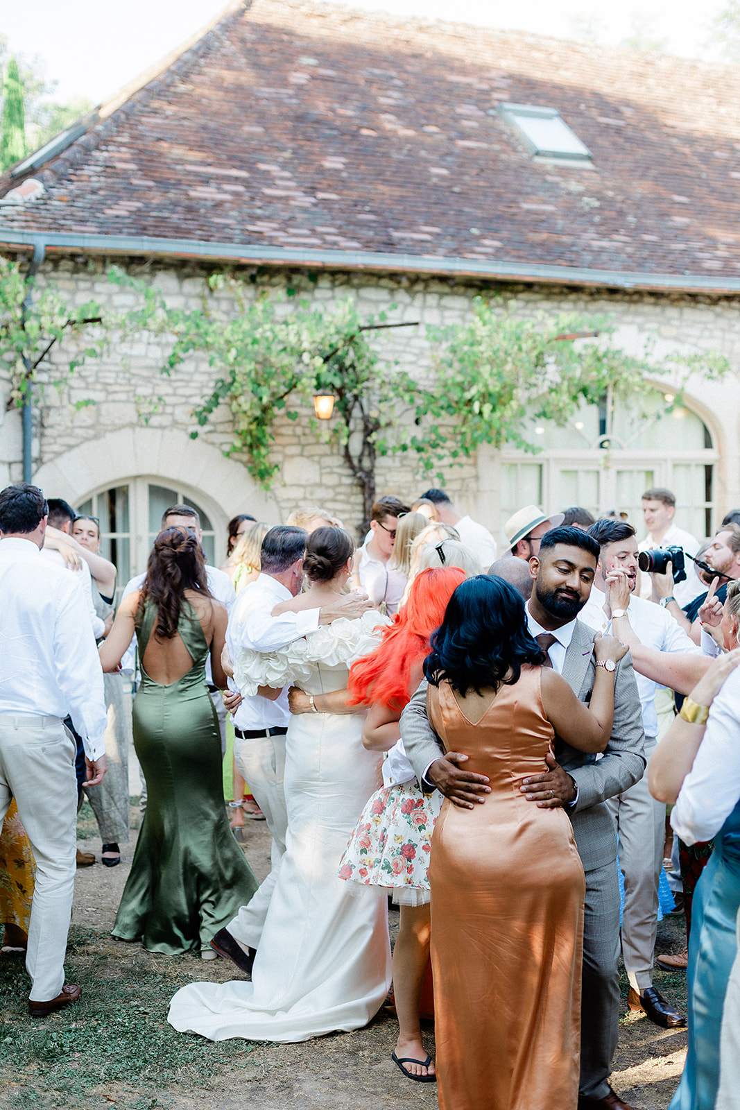 Wedding reception guests dancing and mingling in courtyard with stone building and ivy-covered walls