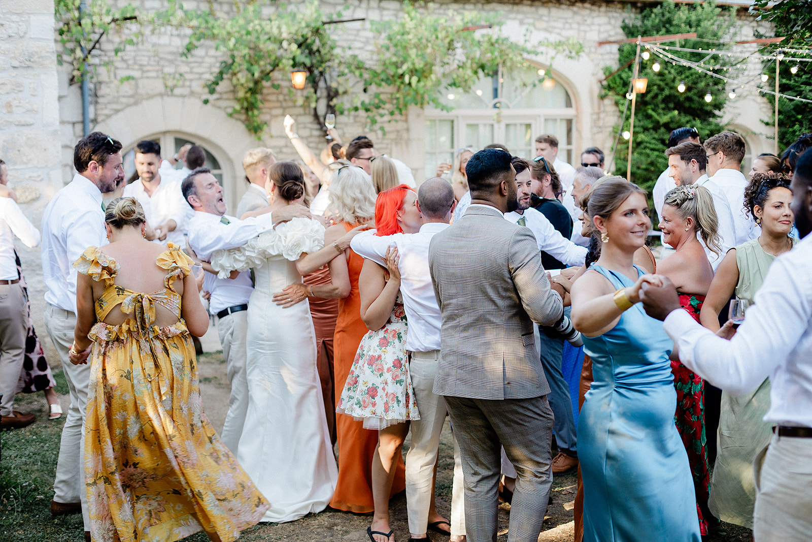 Wedding guests dancing in stone courtyard with string lights and historic architecture