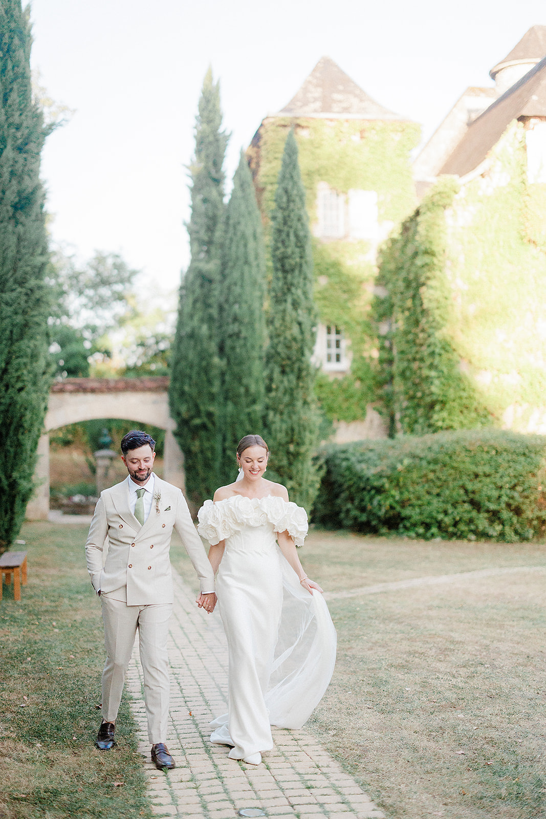 Bride and groom walking hand-in-hand through formal courtyard at European château estate
