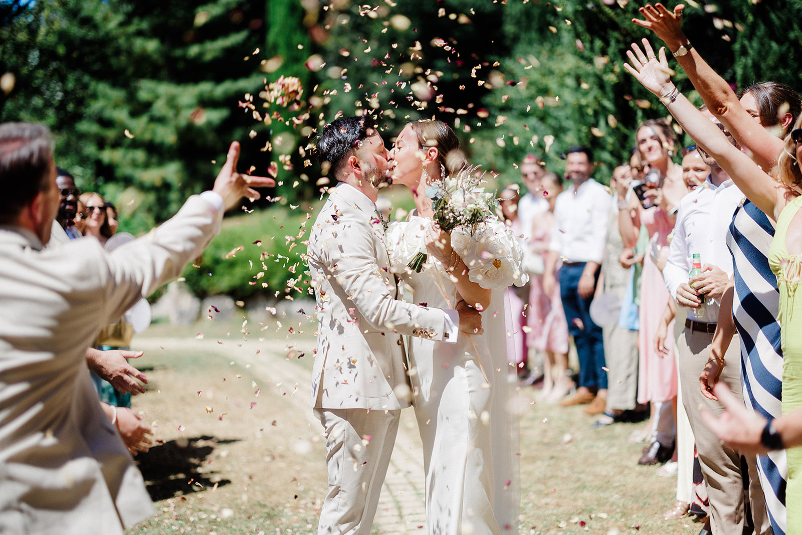 Bride and groom kiss during outdoor ceremony recessional with confetti toss in garden setting