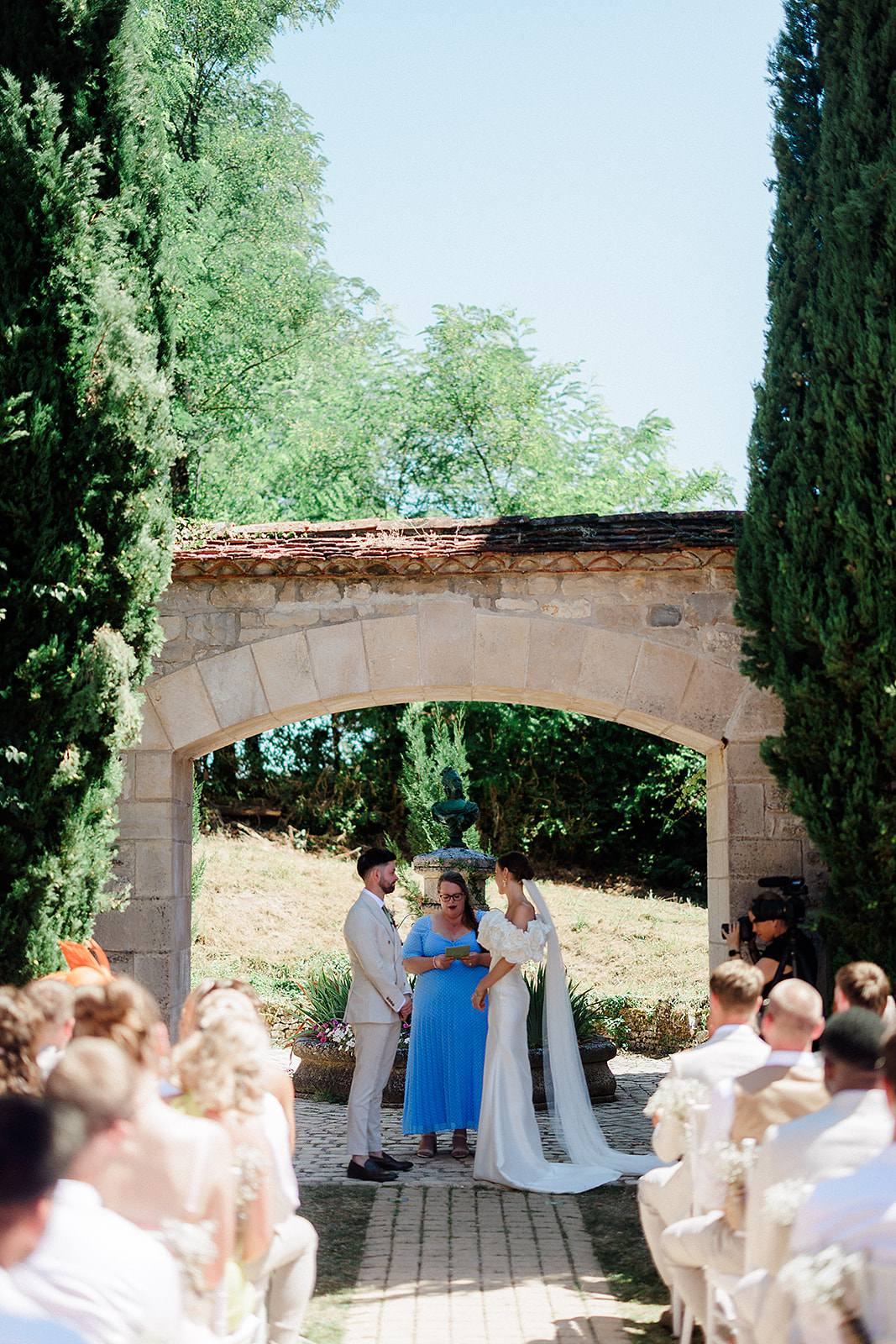 Outdoor wedding ceremony under stone archway with cypress trees at Mediterranean garden venue