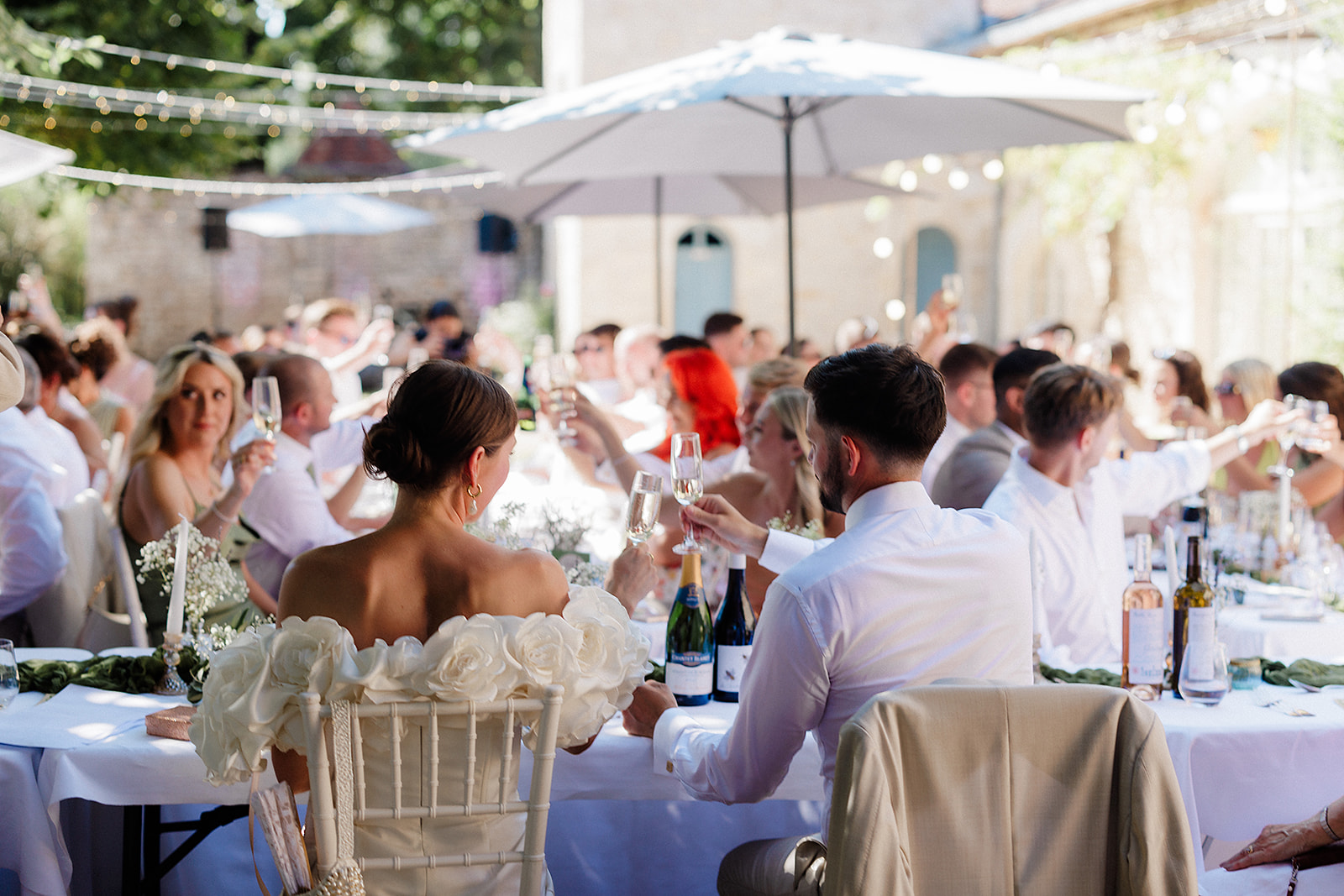 Bride and groom toasting with champagne at outdoor courtyard reception with white linens and ivory roses