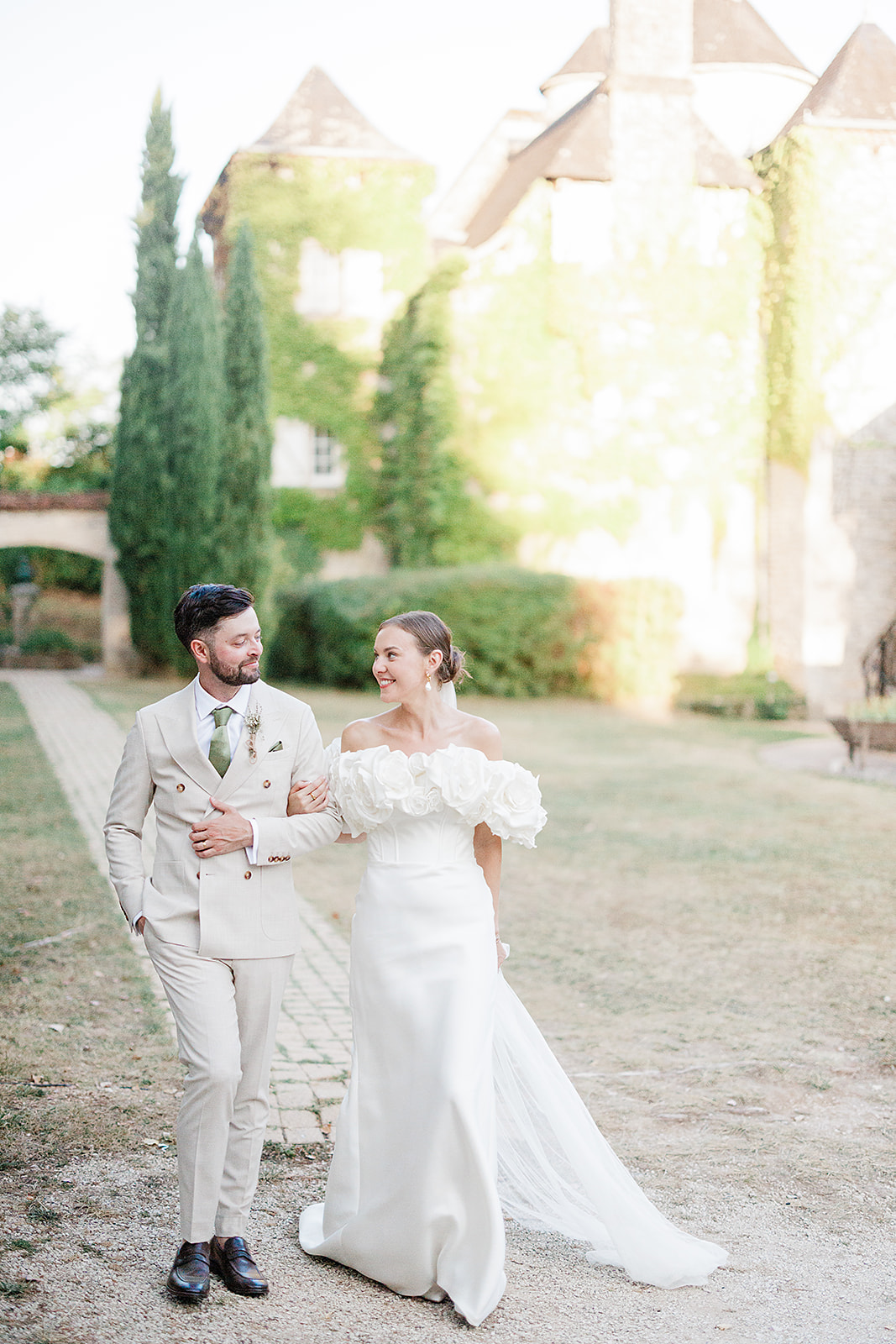 Bride and groom walking together in courtyard of historic stone château during wedding portraits