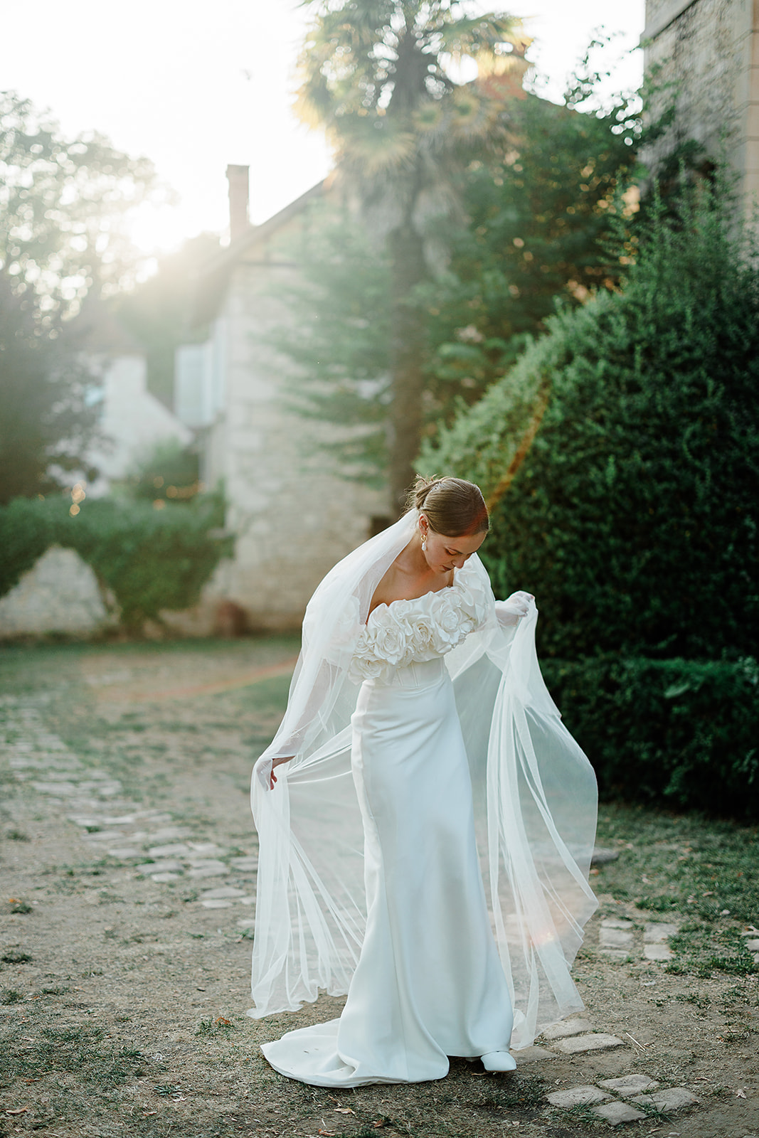 Bride in ivory gown with flowing cape posing in courtyard with ivy-covered stone walls