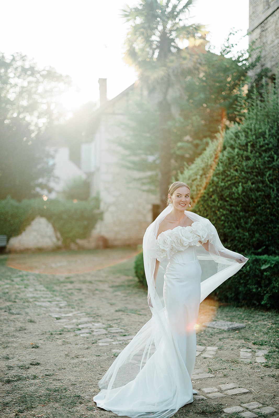 Bride in ivory gown and veil walking through stone courtyard at historic estate