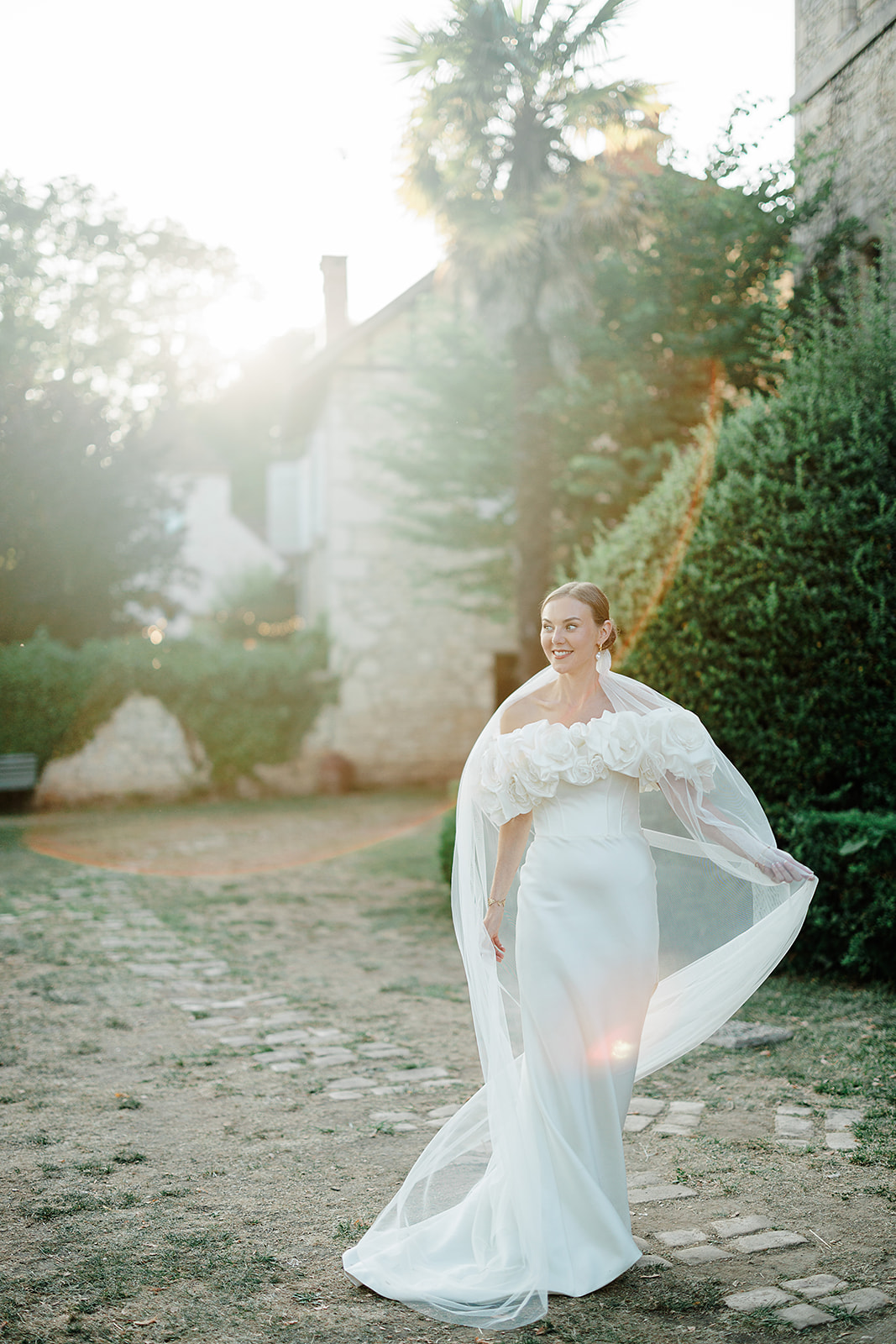 Bride in flowing ivory gown walking through historic stone courtyard during golden hour