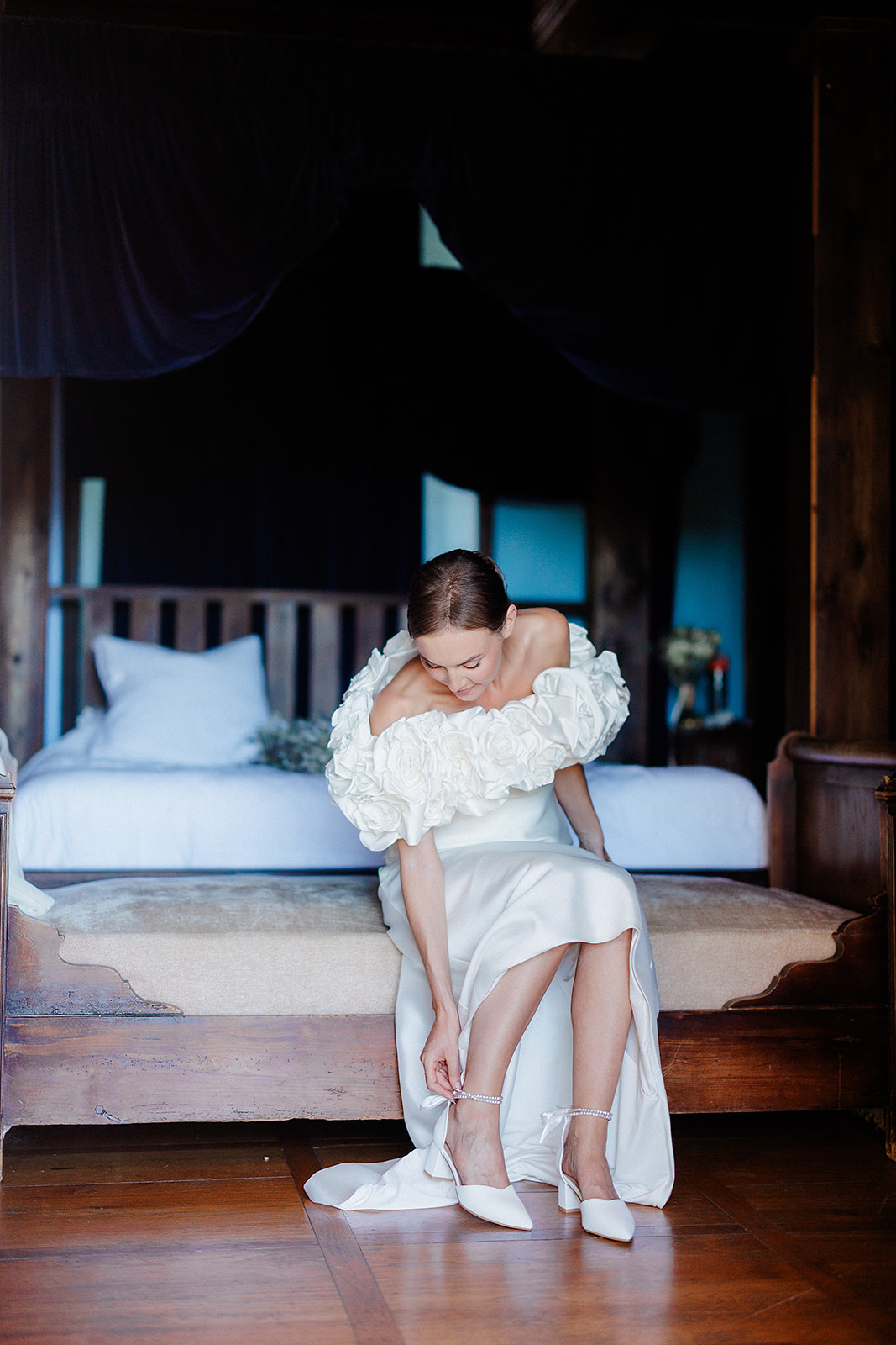 Bride fastening ankle bracelet in ivory dress during getting ready moment in bedroom