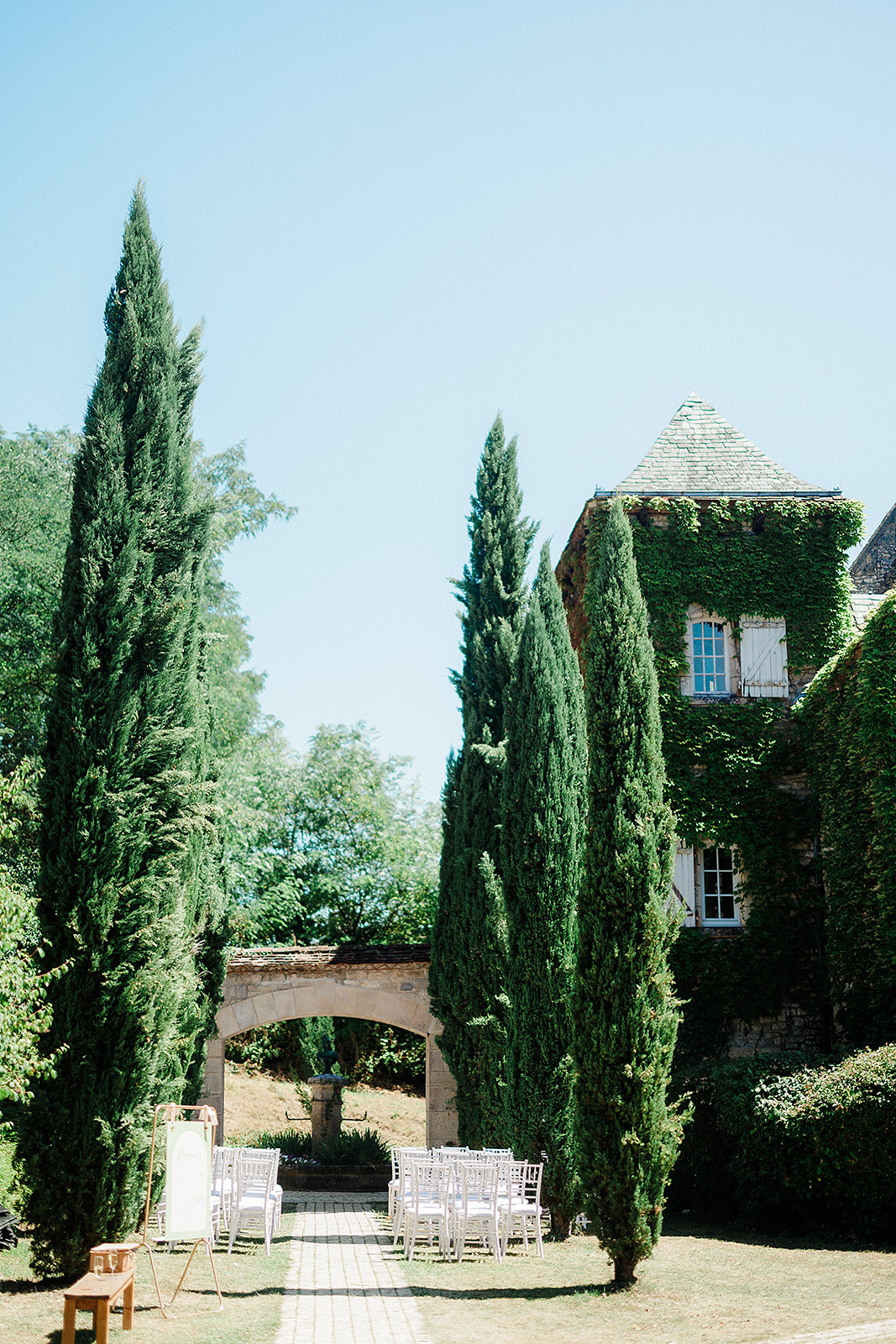 Outdoor wedding ceremony setup in European courtyard with cypress trees and stone architecture